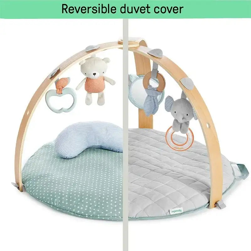 Front of Ingenuity Cozy Spot activity gym showing reversible duvet (mint star and gray quilt) and wooden toy arch on white