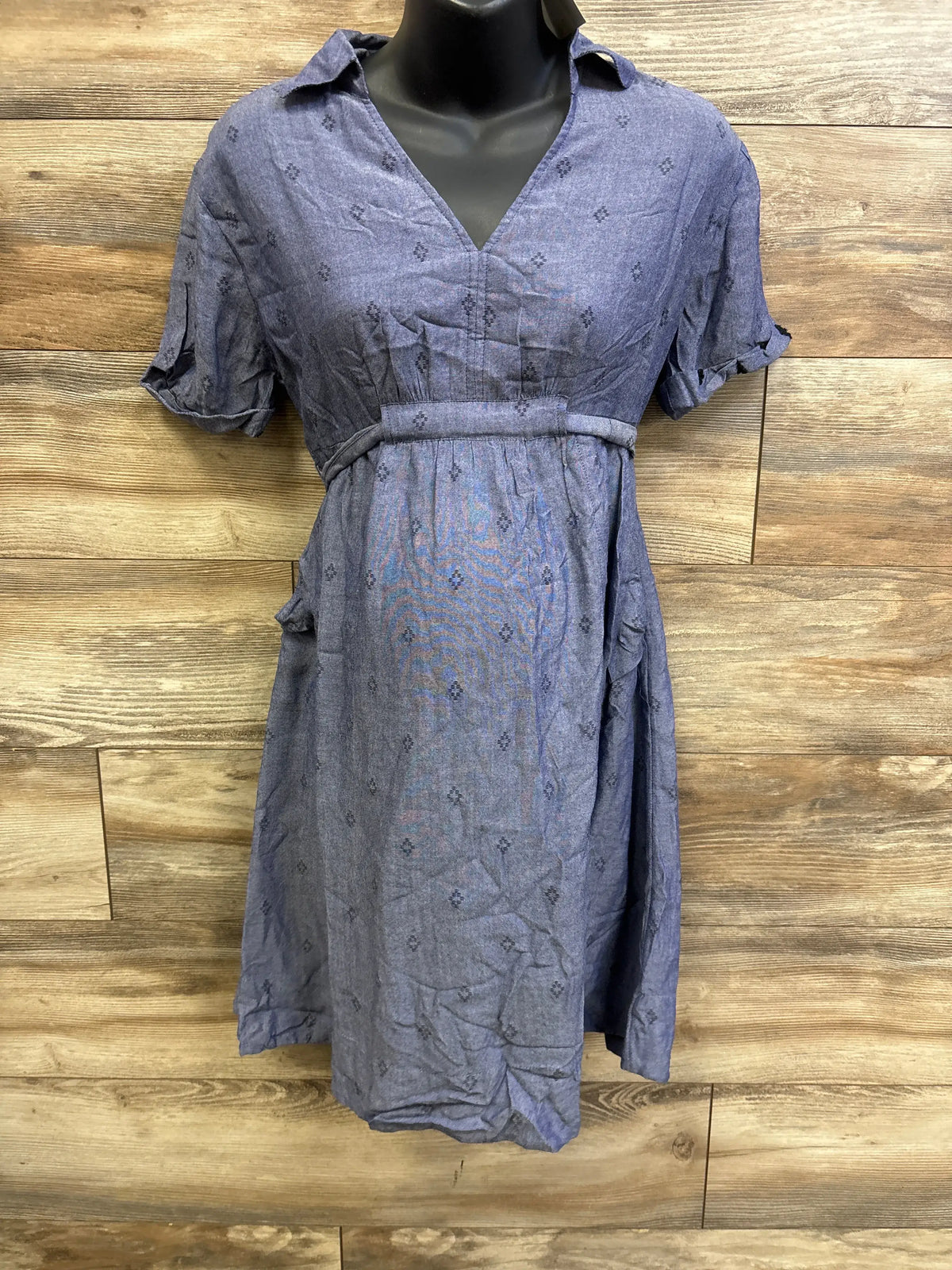 Front of blue chambray shirtdress with V-neck, empire waist belt and cuffed short sleeves on mannequin against wood backdrop