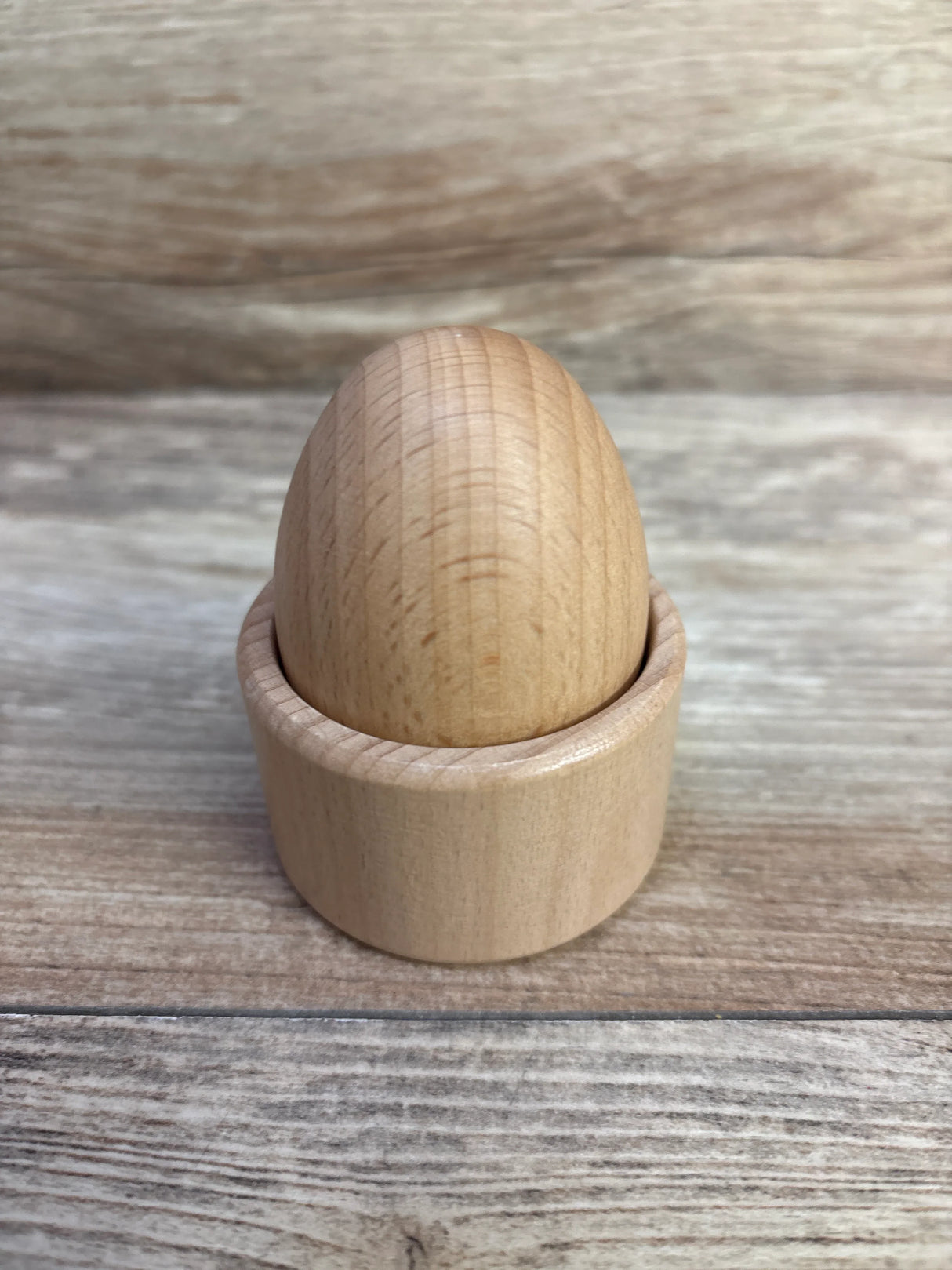 Smooth wooden egg sitting in a matching wooden egg cup on wood surface