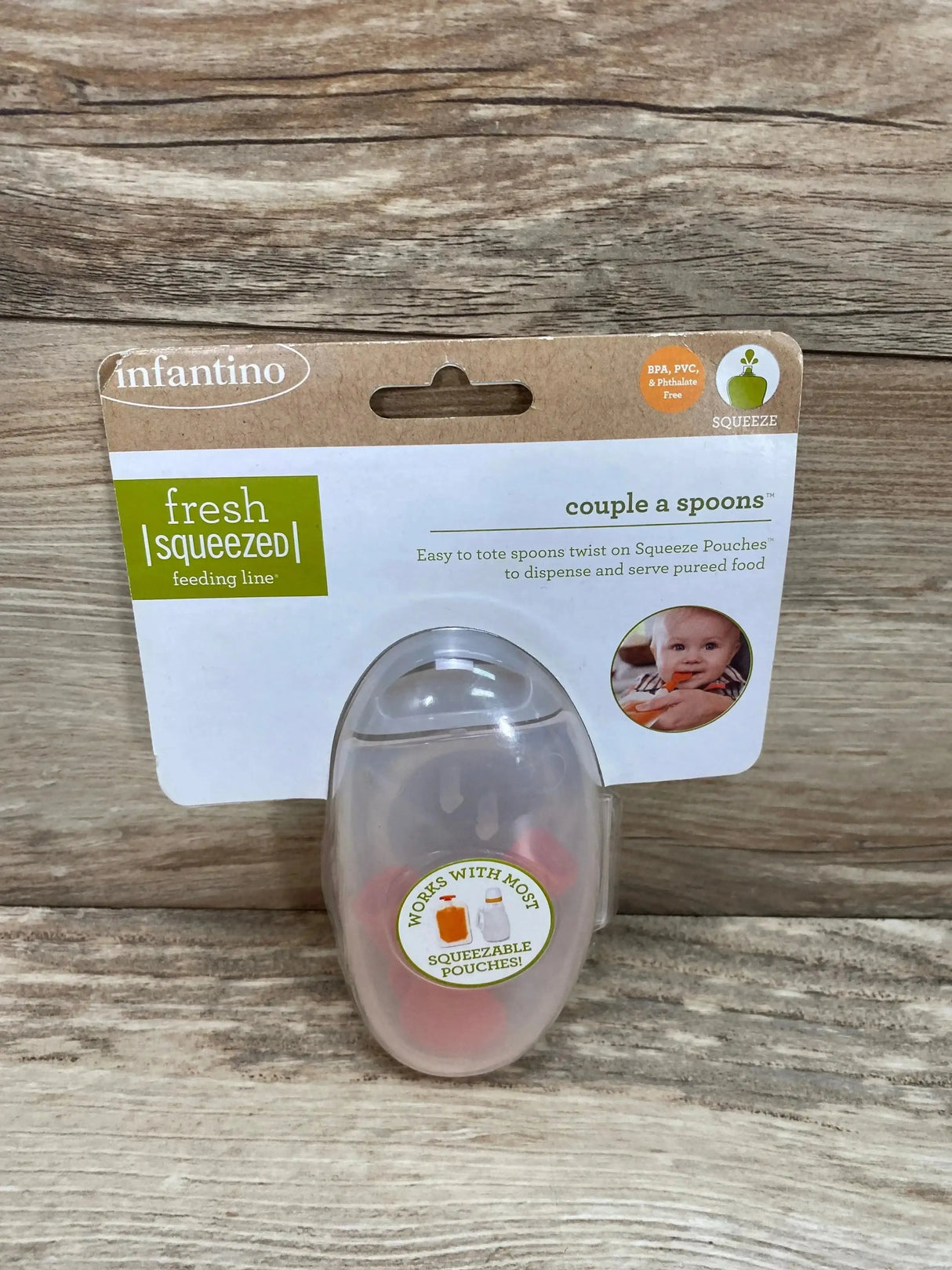Front view of Infantino Couple-a-Spoons package showing two twist-on feeding spoons in clear oval case against wood background