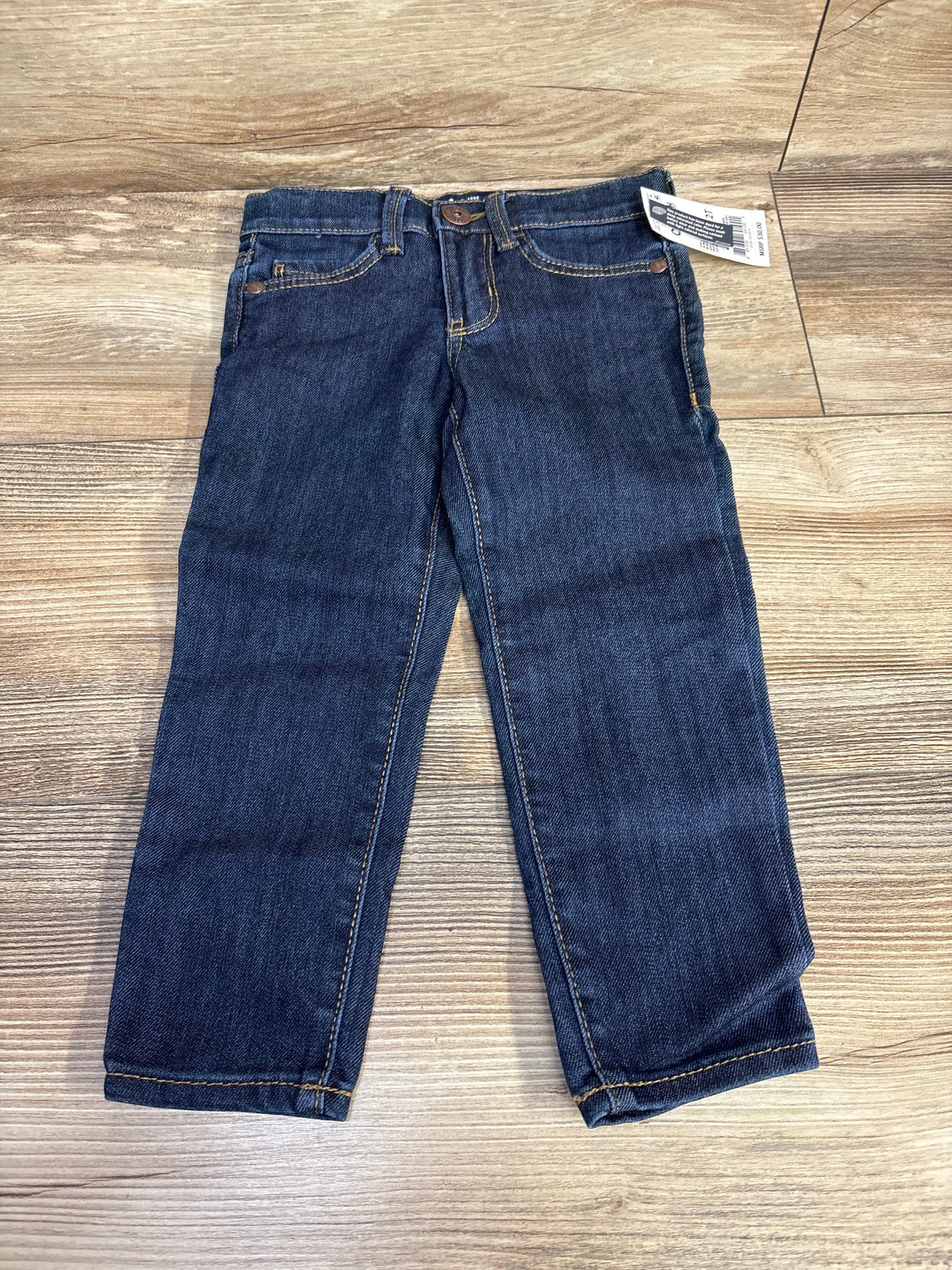 Dark blue kids jeans with front pockets and a tag, laid flat on wooden floor