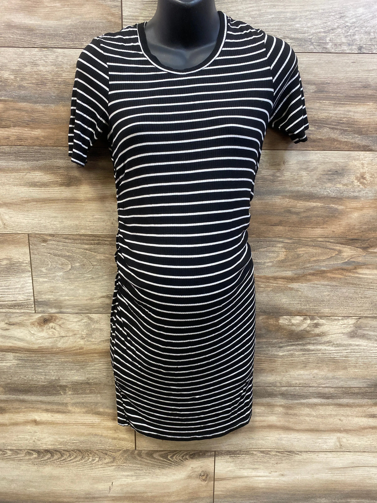 Front view of black maternity striped ruched dress showcasing short sleeves and ruched sides against a wood floor