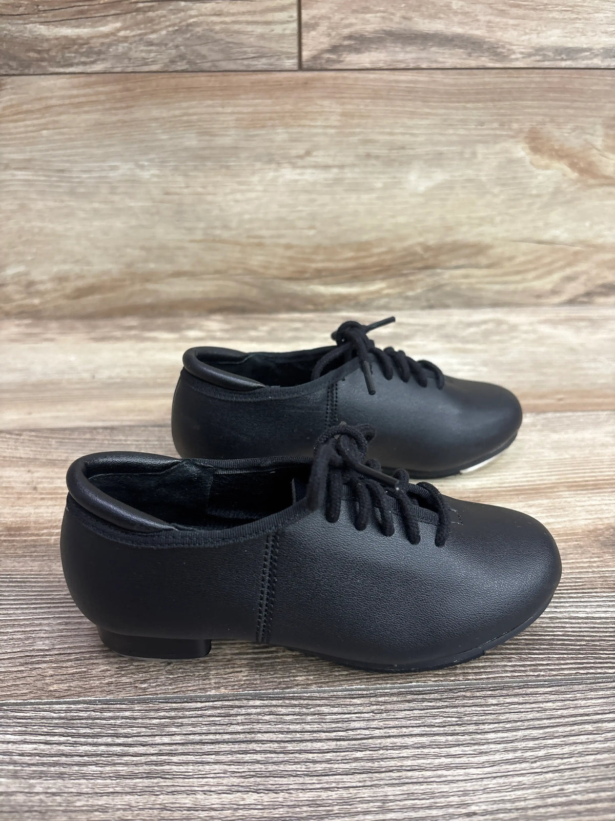 Pair of black lace-up theatricals tap shoes for children on a wooden floor