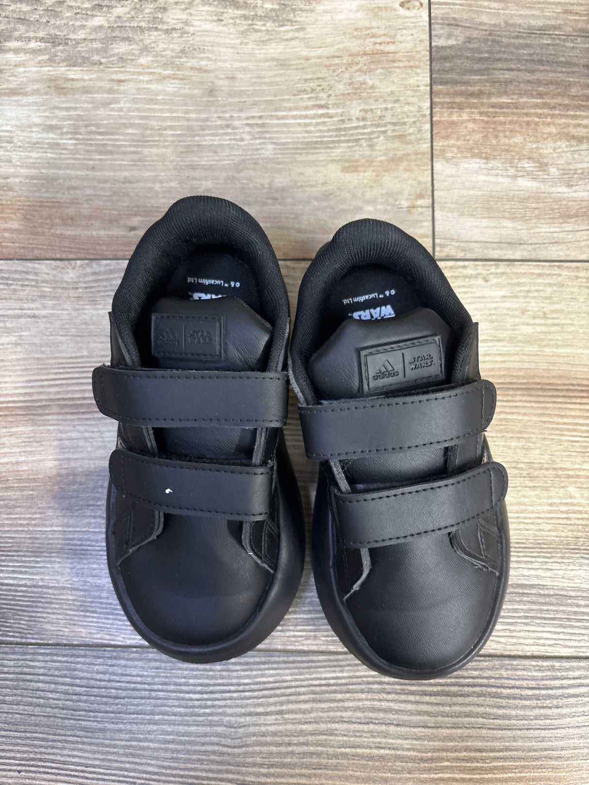 Top view of toddler black Adidas Star Wars Bubblecomfy double-strap sneakers with two Velcro straps on light wood floor
