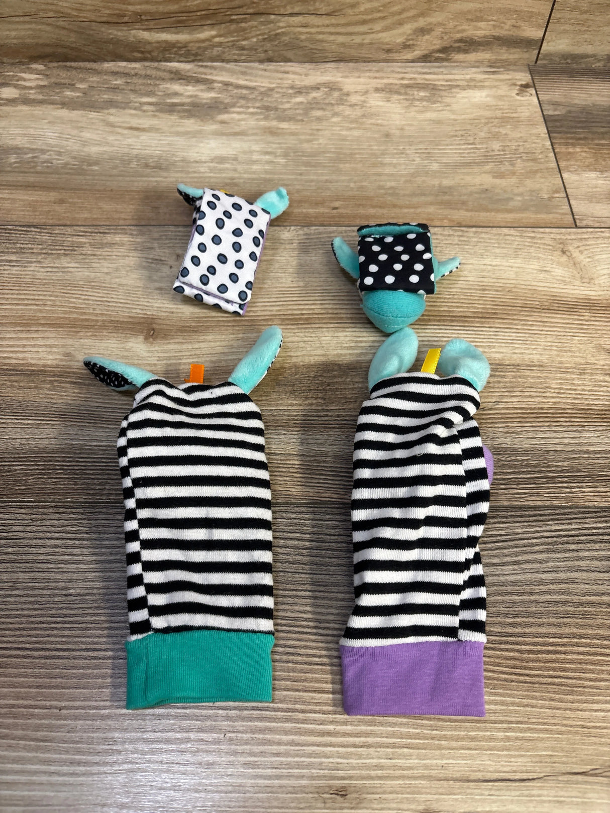 Top-down view of baby wrist rattles and foot finders with black-and-white stripes, teal and purple cuffs on wood background