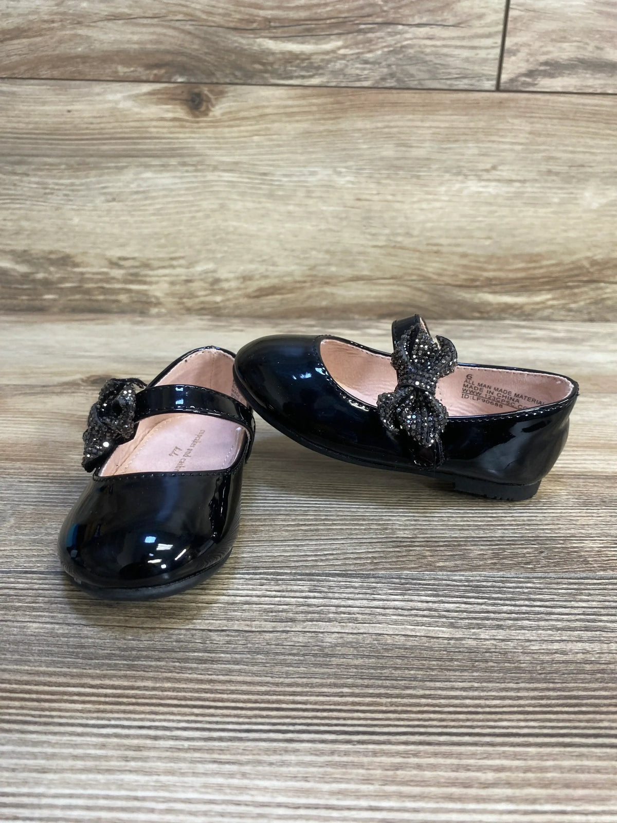 Black patent leather toddler girl dress shoes with beaded bow on wooden floor