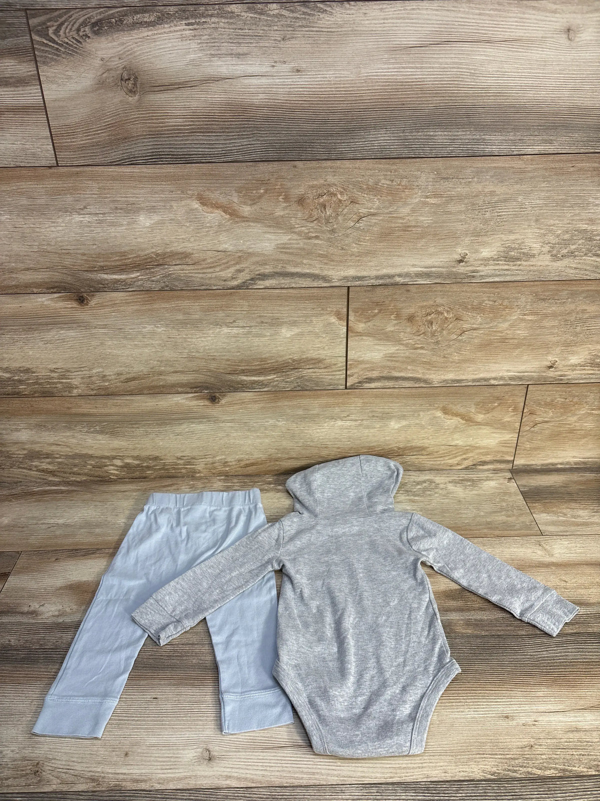 Back view of Carter’s two-piece dinosaur hooded bodysuit set in grey, showing long sleeves and matching pants on a wood floor