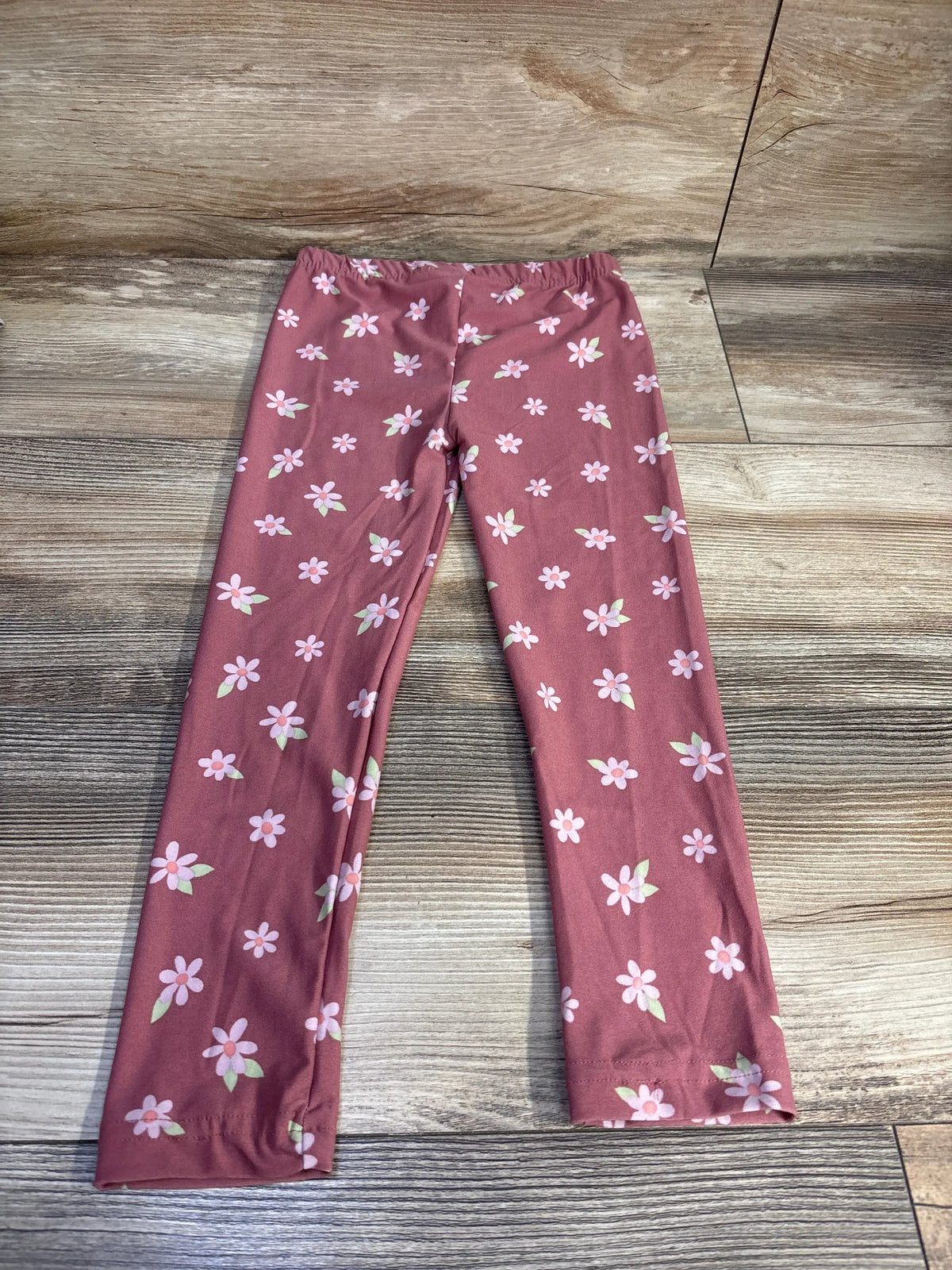Top-down view of Derek Heart floral leggings in pink with an all-over flower pattern on a wood floor