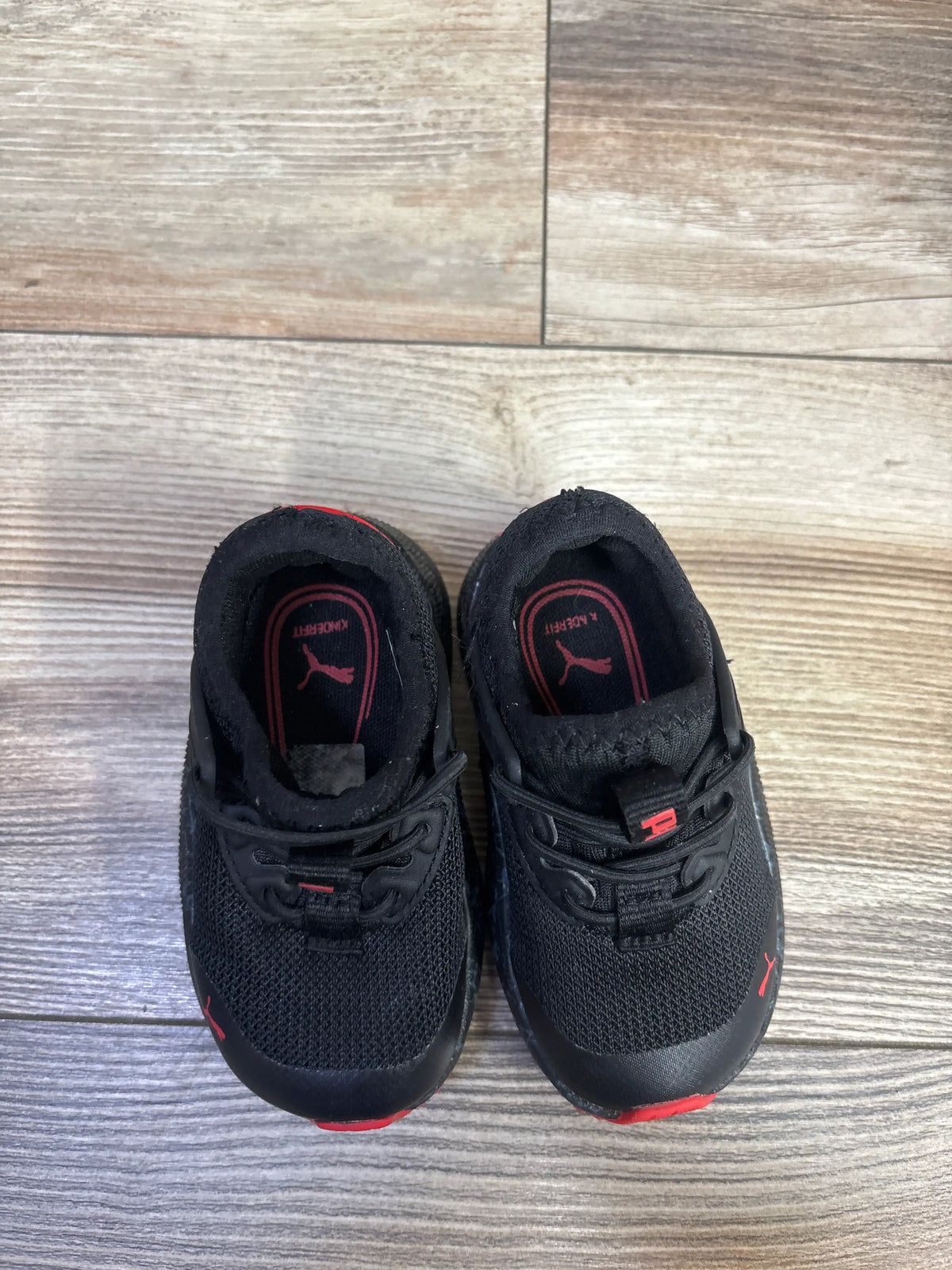 Top view of Puma Pacer Marbleized AC PS sneakers showcasing black mesh uppers and red accents on a wood floor