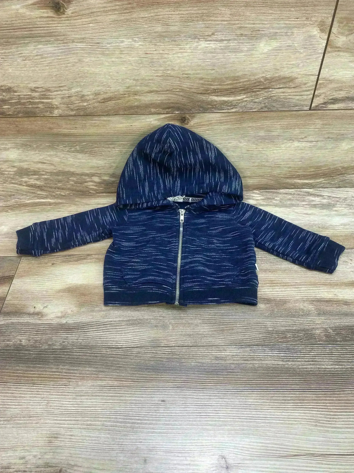 Front view of navy full-zip baby hoodie size 12m with hood, silver zipper, and white heathered streaks on wood floor