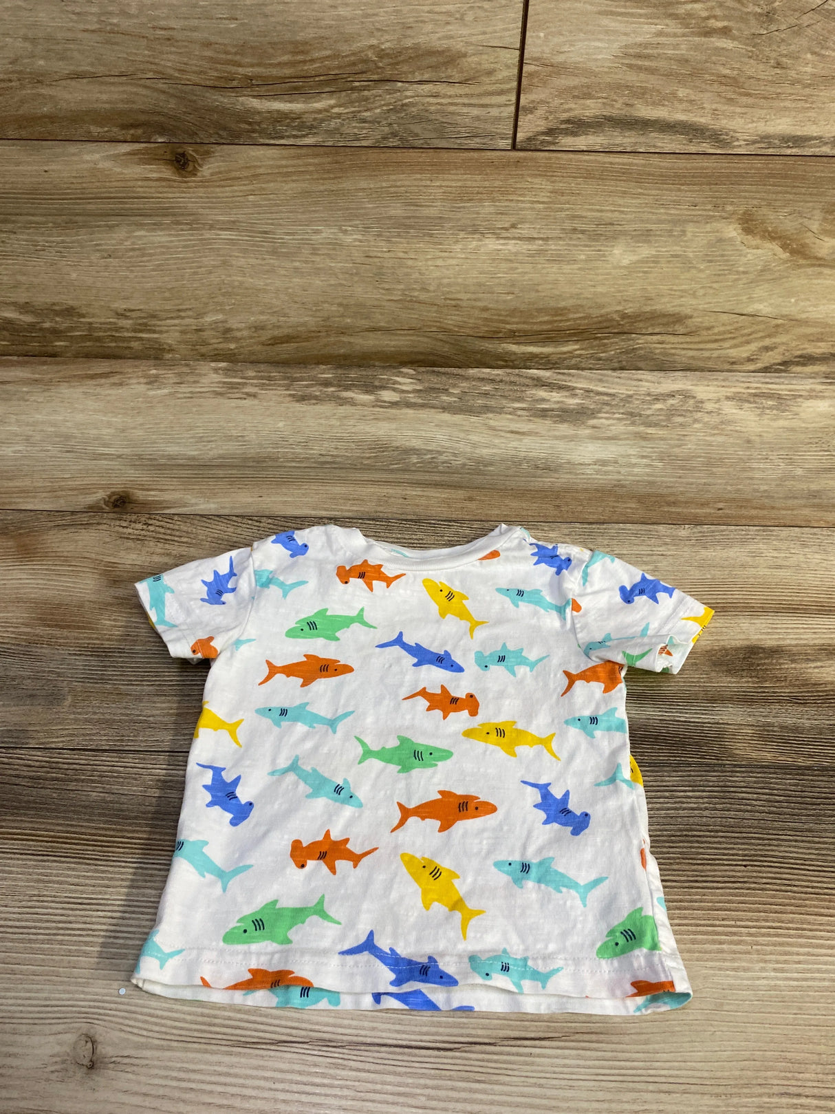 Back view of Little Me white short sleeve toddler shirt showcasing multicolored shark print on wood background