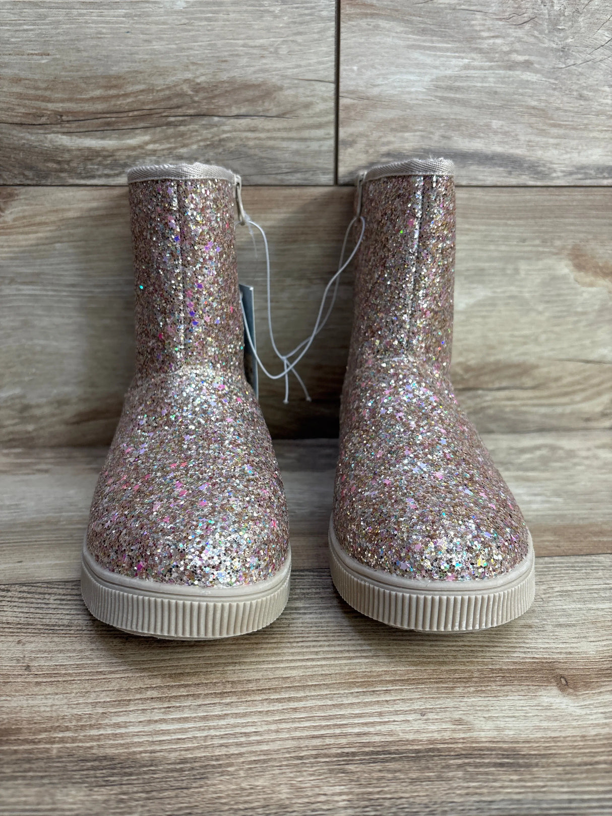 Sparkly pink glitter kids boots with rubber soles on wood background
