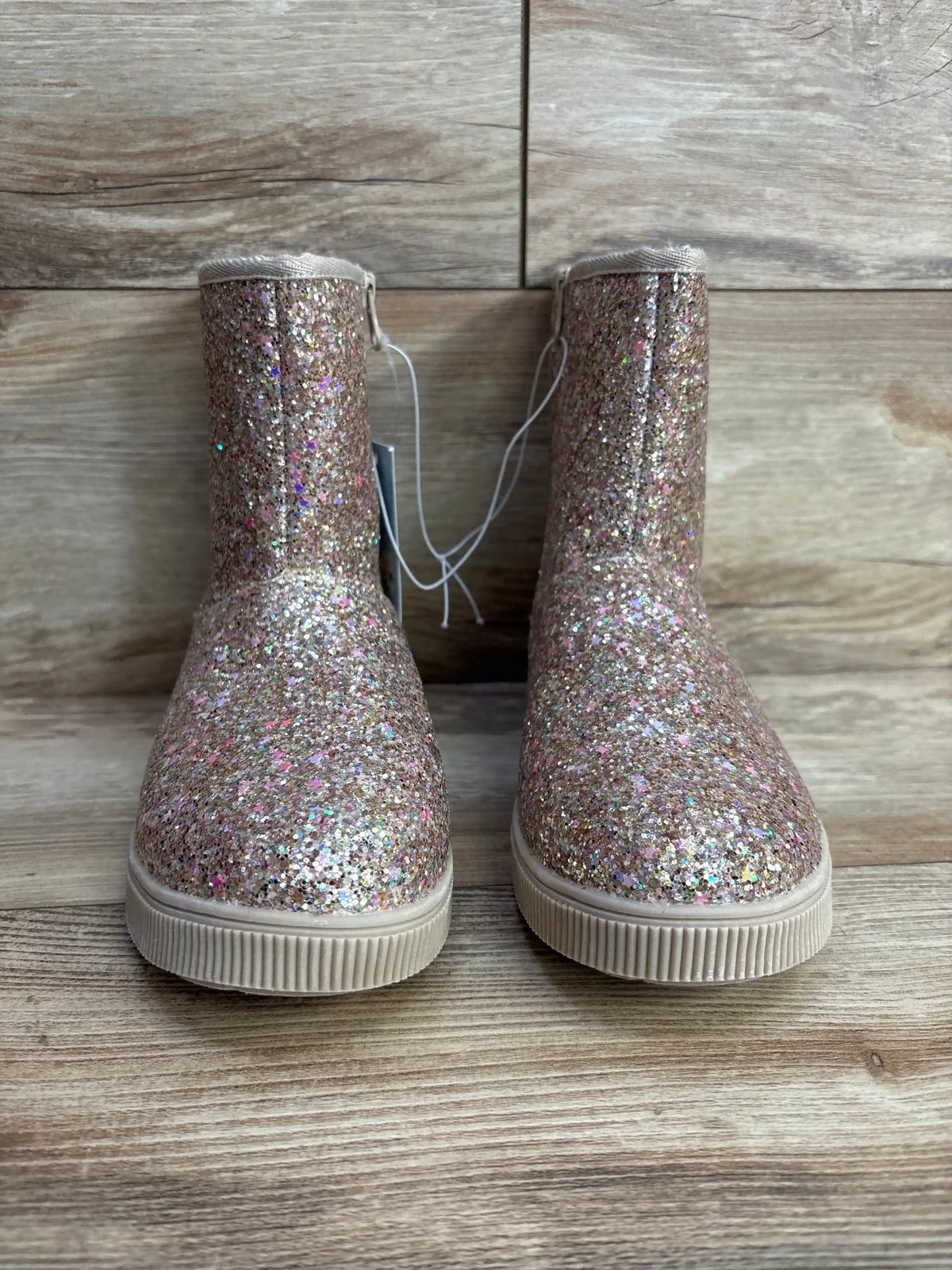 Front view of Cat & Jack Holland shearling-style kids boots showcasing glittery gold finish and rubber soles on wood background