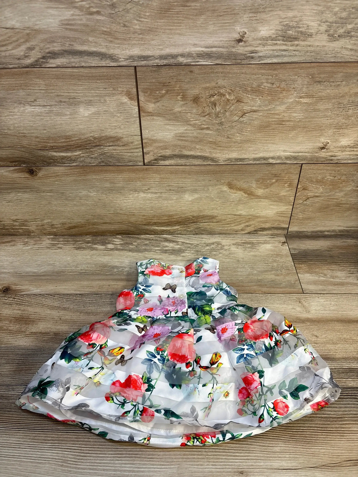 Front view of white sleeveless baby dress from a two piece set showcasing layered floral and butterfly print on wood floor