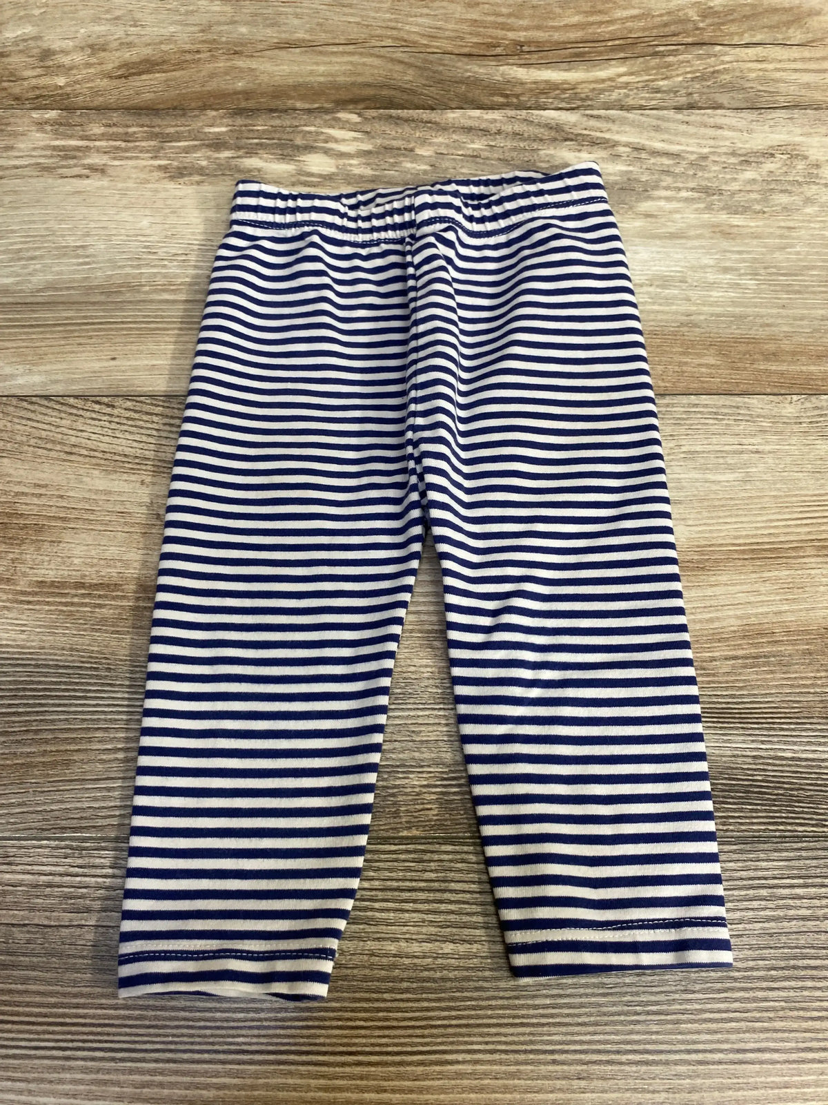 Top-down view of baby navy and white striped leggings showing elastic waistband and full length legs on wood background