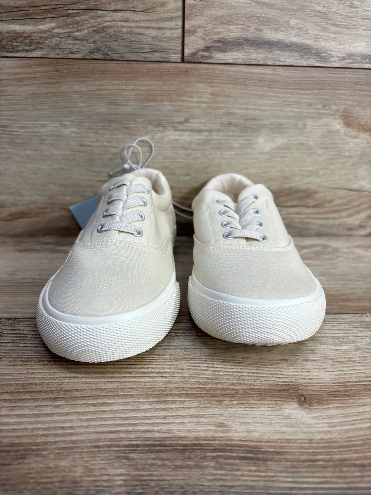 Pair of beige canvas kids sneakers with white rubber soles on wooden floor