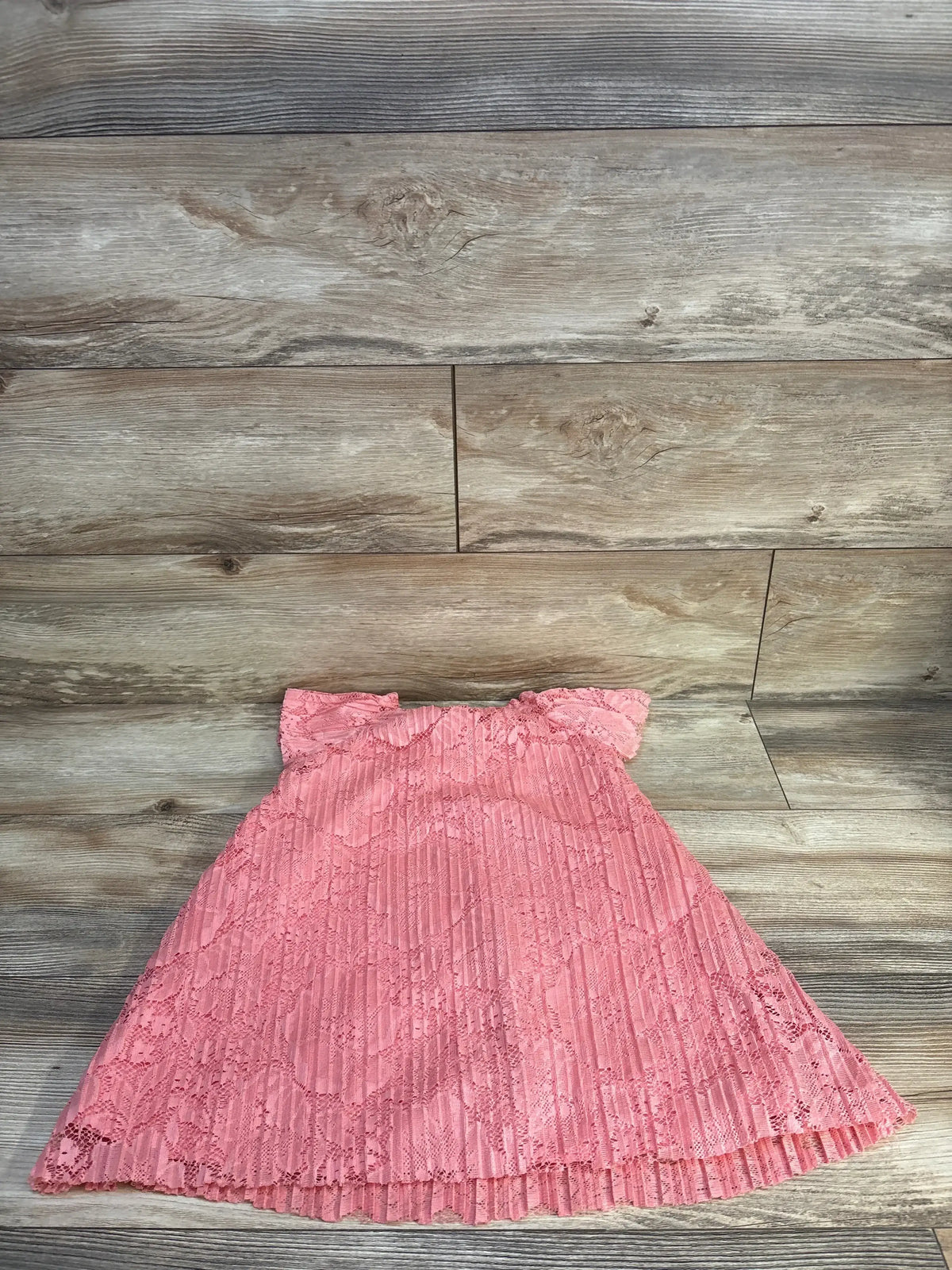 Pink lace baby dress with ruffled sleeves and pleated skirt on wood floor