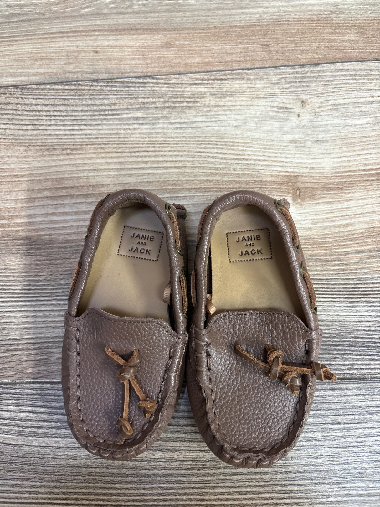 Pair of brown Janie and Jack leather moccasin baby shoes on wood floor