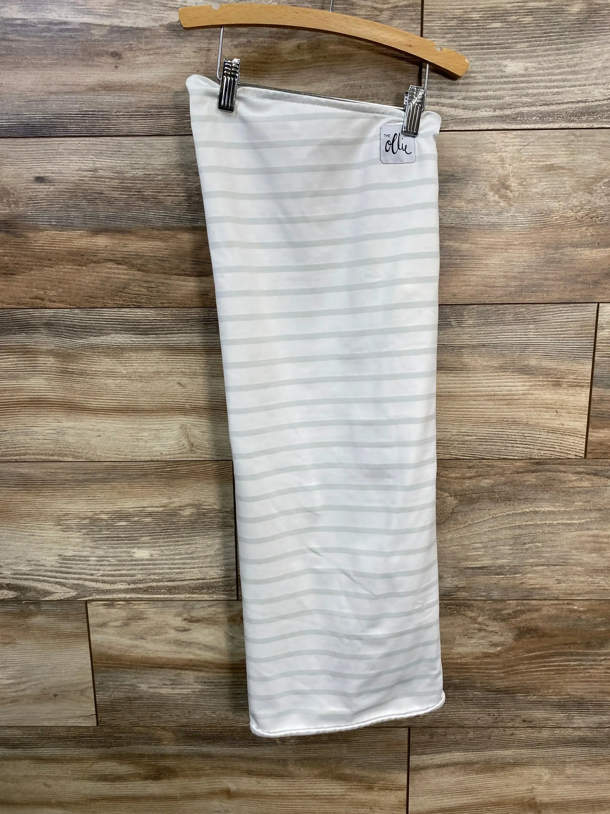 Front view of white baby swaddle with light gray stripes and brand tag on a wooden hanger against wood-plank background