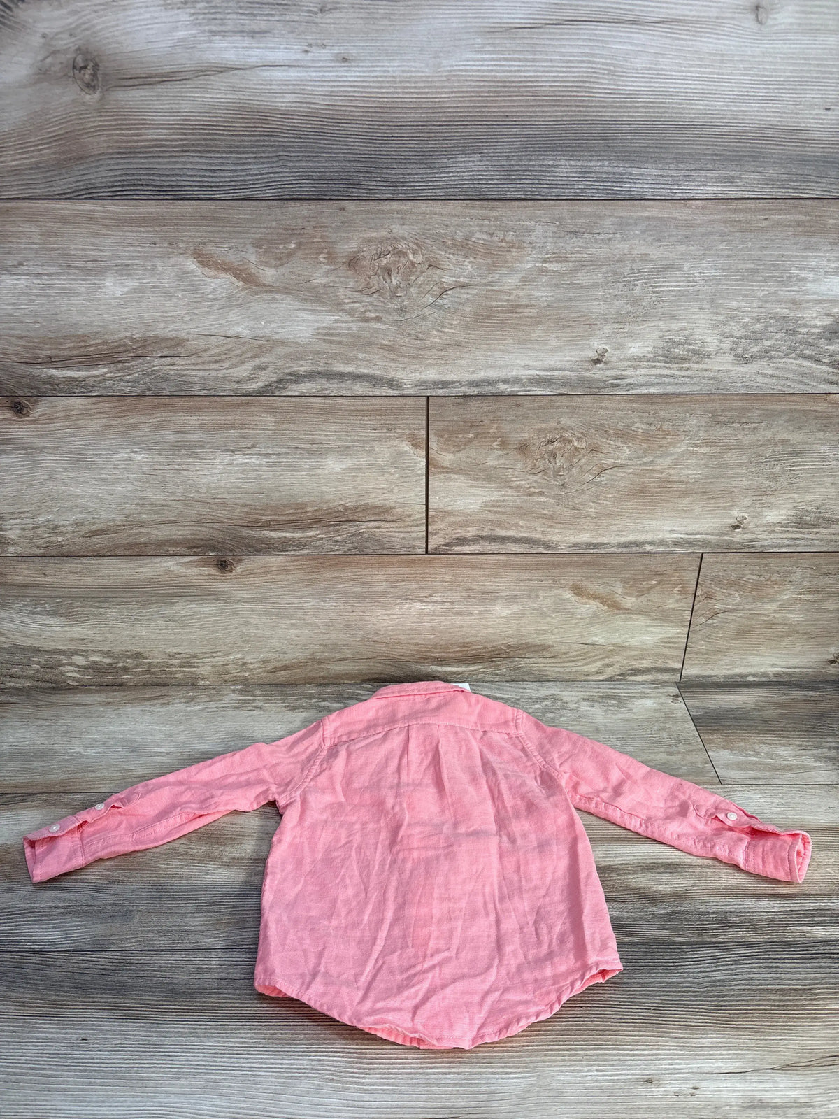 Back view of pink Janie & Jack long-sleeve button-up shirt, size 2T, with buttoned cuffs on a wood background