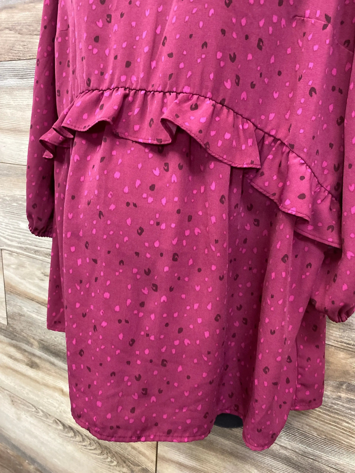 Front close-up of burgundy maternity ruffled blouse (medium) showing ruffle waist, pink spot print, and long sleeves on wood background