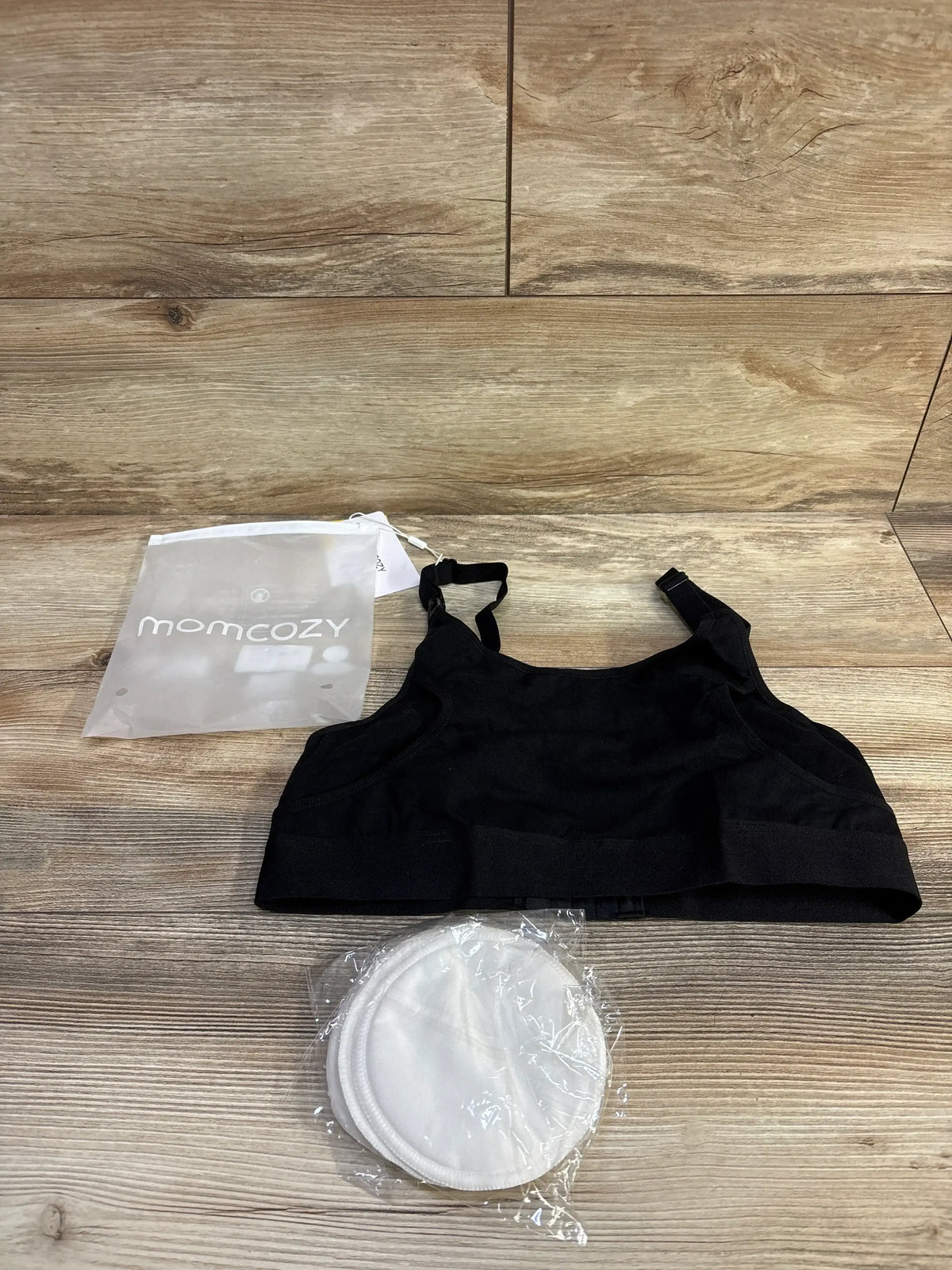 Top-down view of Momcozy hands-free pumping bra with packaged white nursing inserts on light wood background