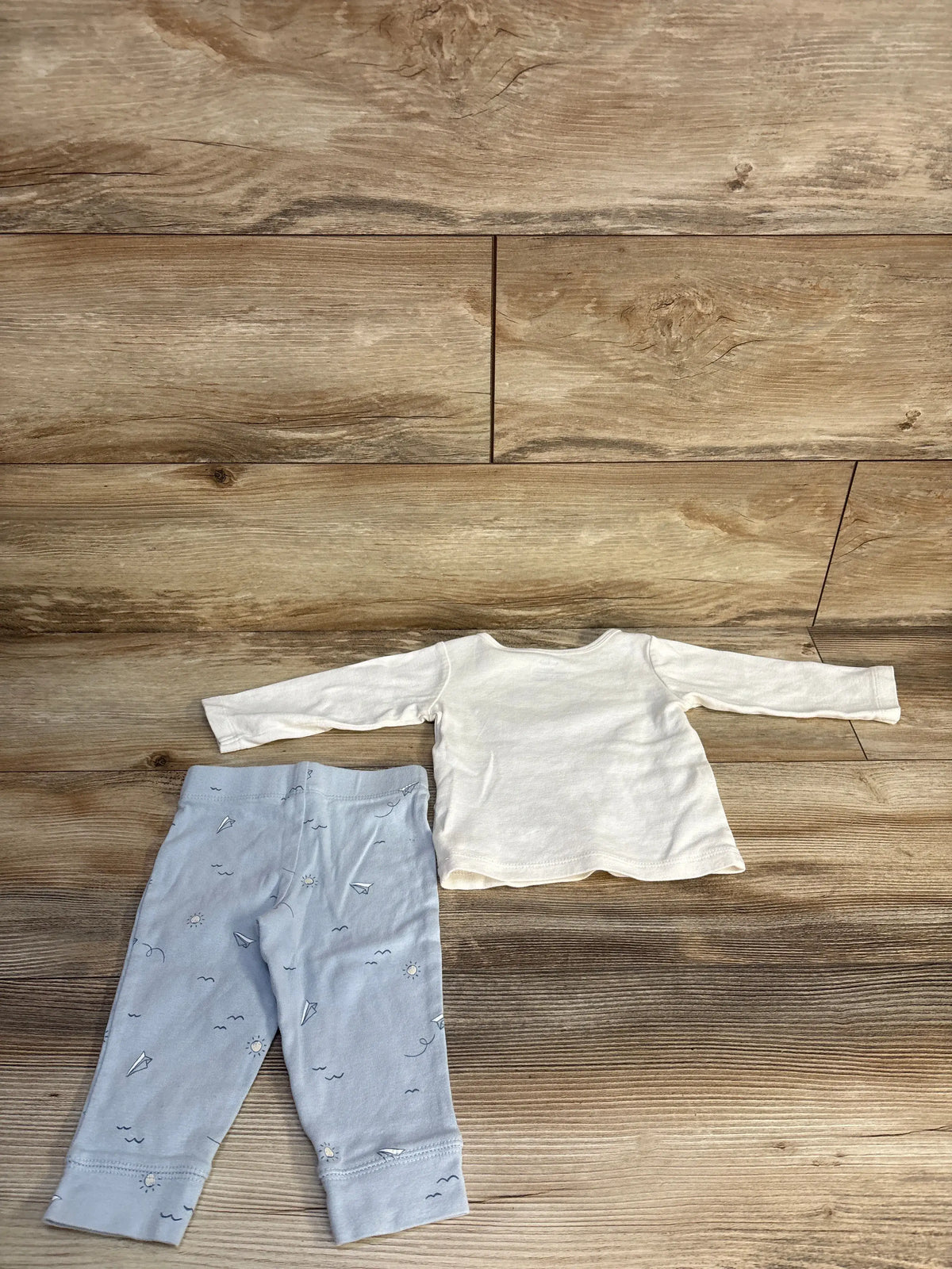 Top view of Carter’s two-piece baby outfit set showing white long-sleeve shirt and patterned pants on wood flooring