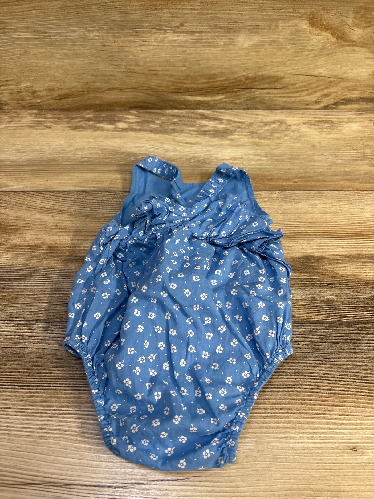 Flat lay of Baby Gap blue sleeveless bubble romper (6–12 months) showing white floral print and ruffle front on wood background
