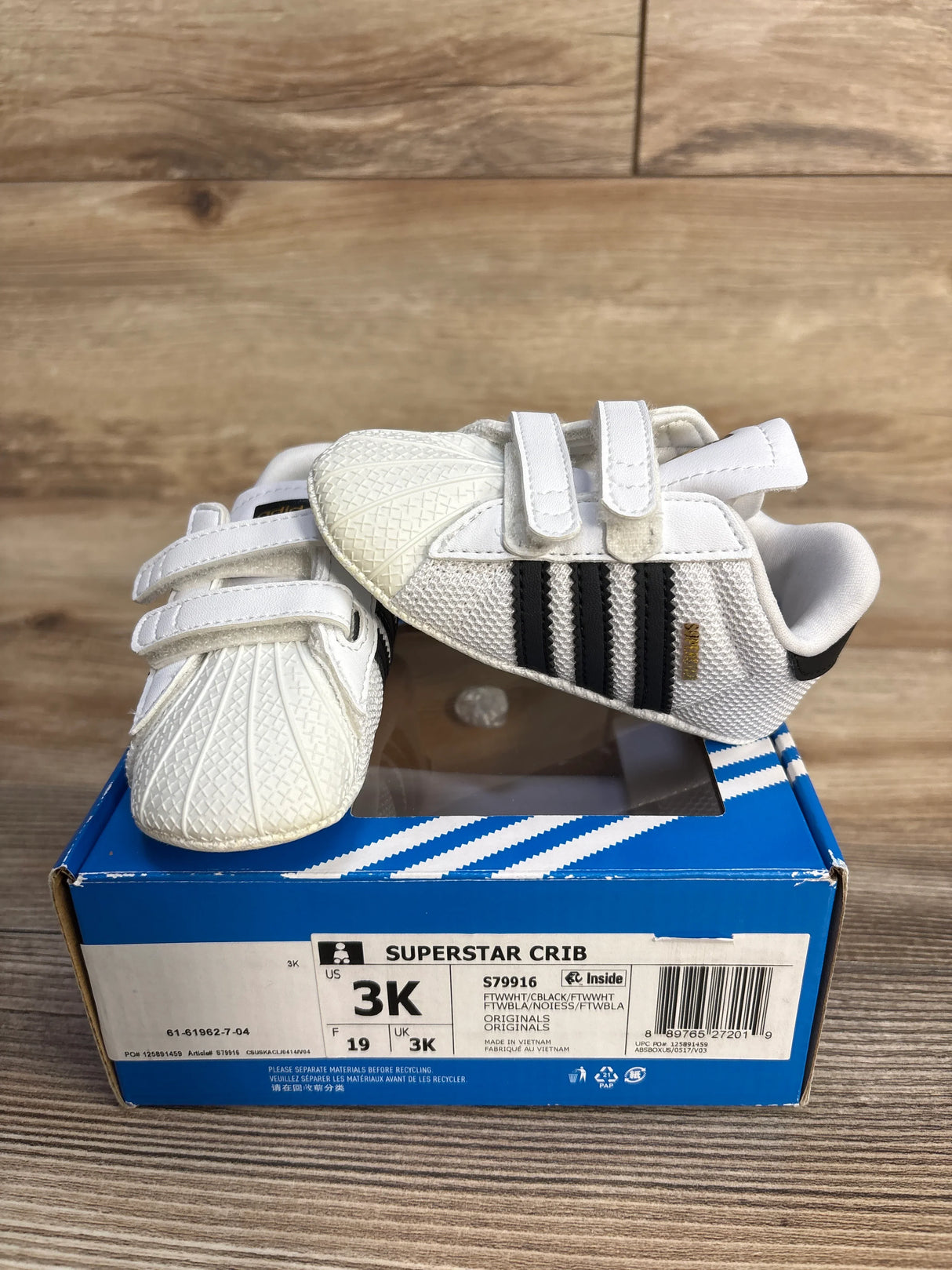 Adidas Superstar Crib baby shoes white with black stripes on blue box, wood background