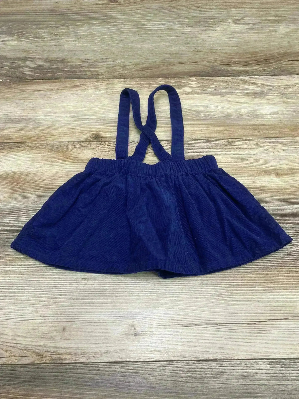 Front view of navy corduroy suspender skirt size 12M showing adjustable button straps and A-line shape on white background