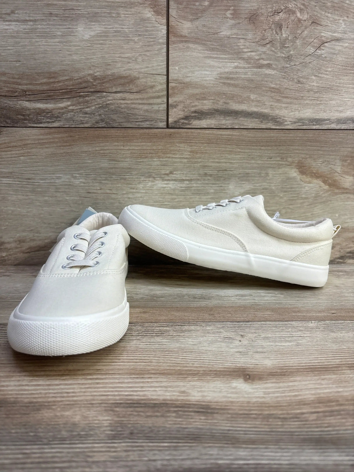 Three-quarter view of Cat and Jack Tyler off-white slip-on kids sneakers with canvas upper and white rubber sole on wood