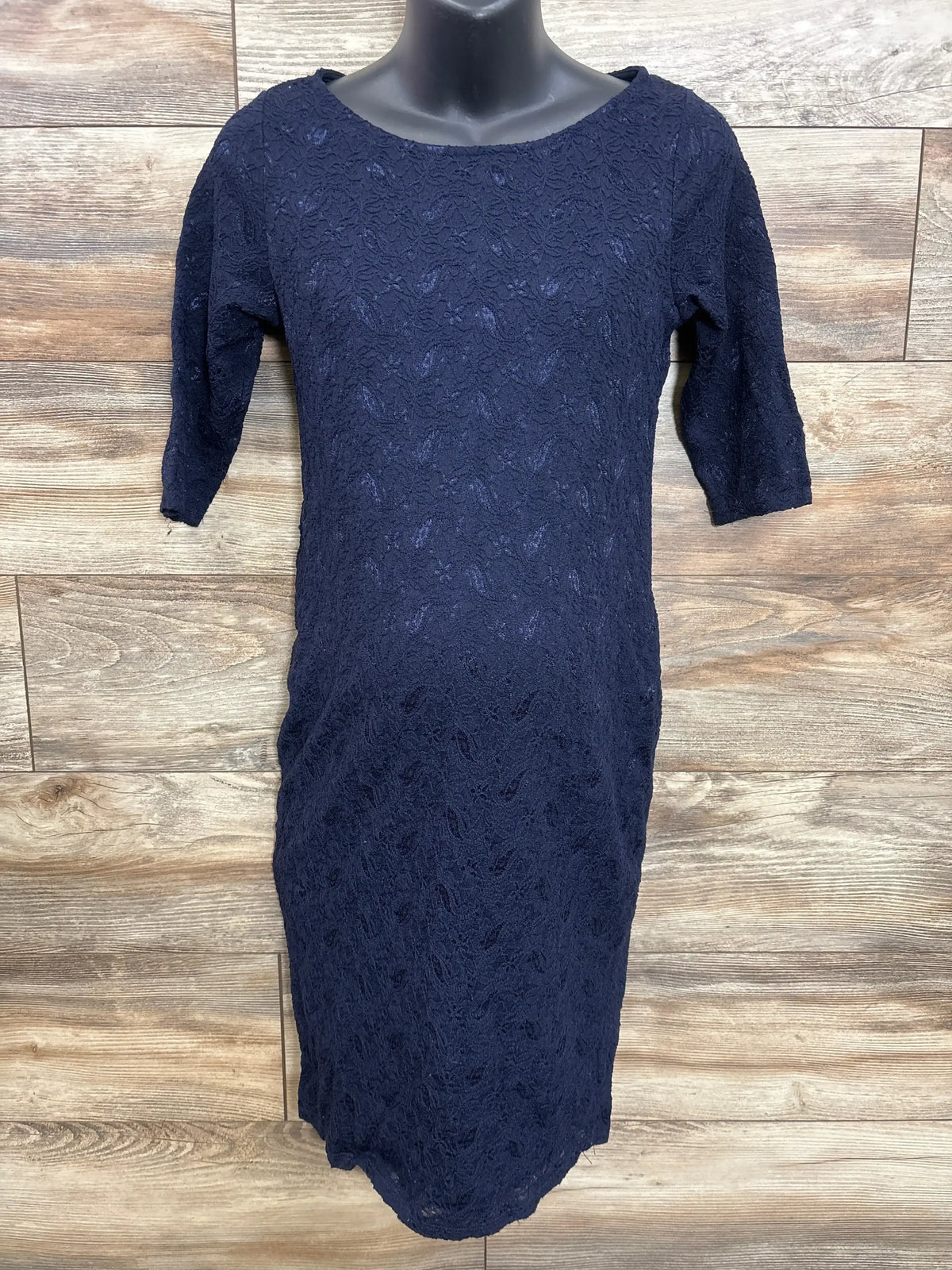 Front of Pink Blush navy maternity fitted lace dress with three-quarter sleeves, on black mannequin against wood background