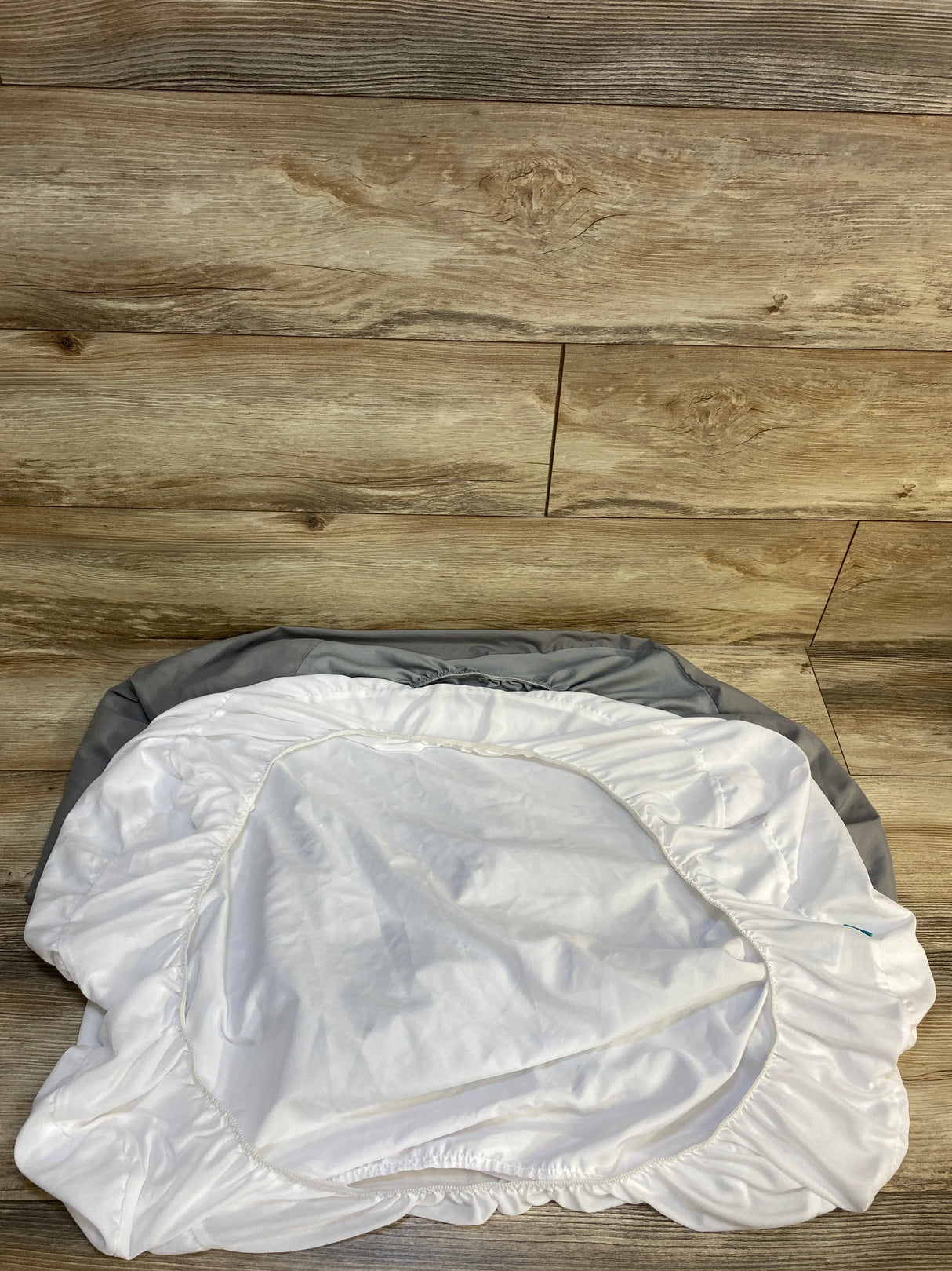 White and gray fitted baby crib sheet on wooden floor, elastic edges visible, nursery bedding