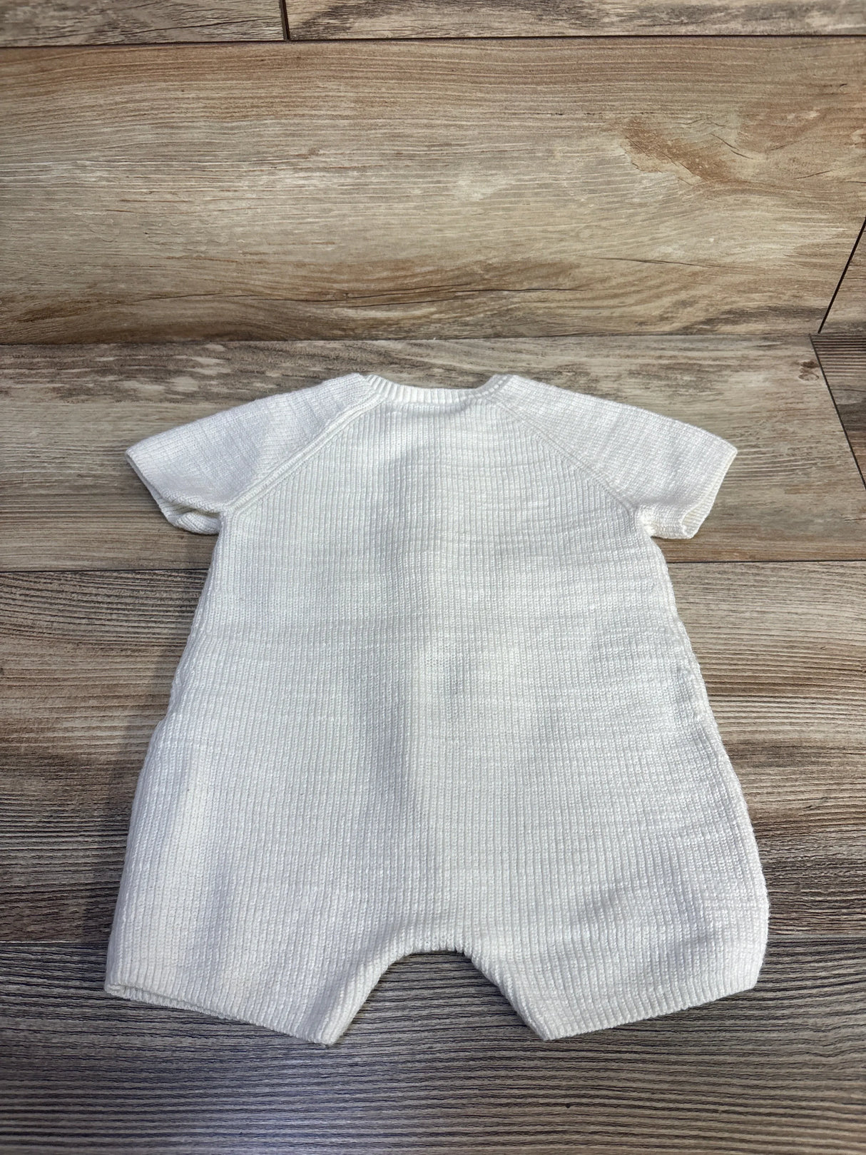 Back view of ivory knit shortie romper showcasing ribbed texture and short raglan sleeves on wood plank background