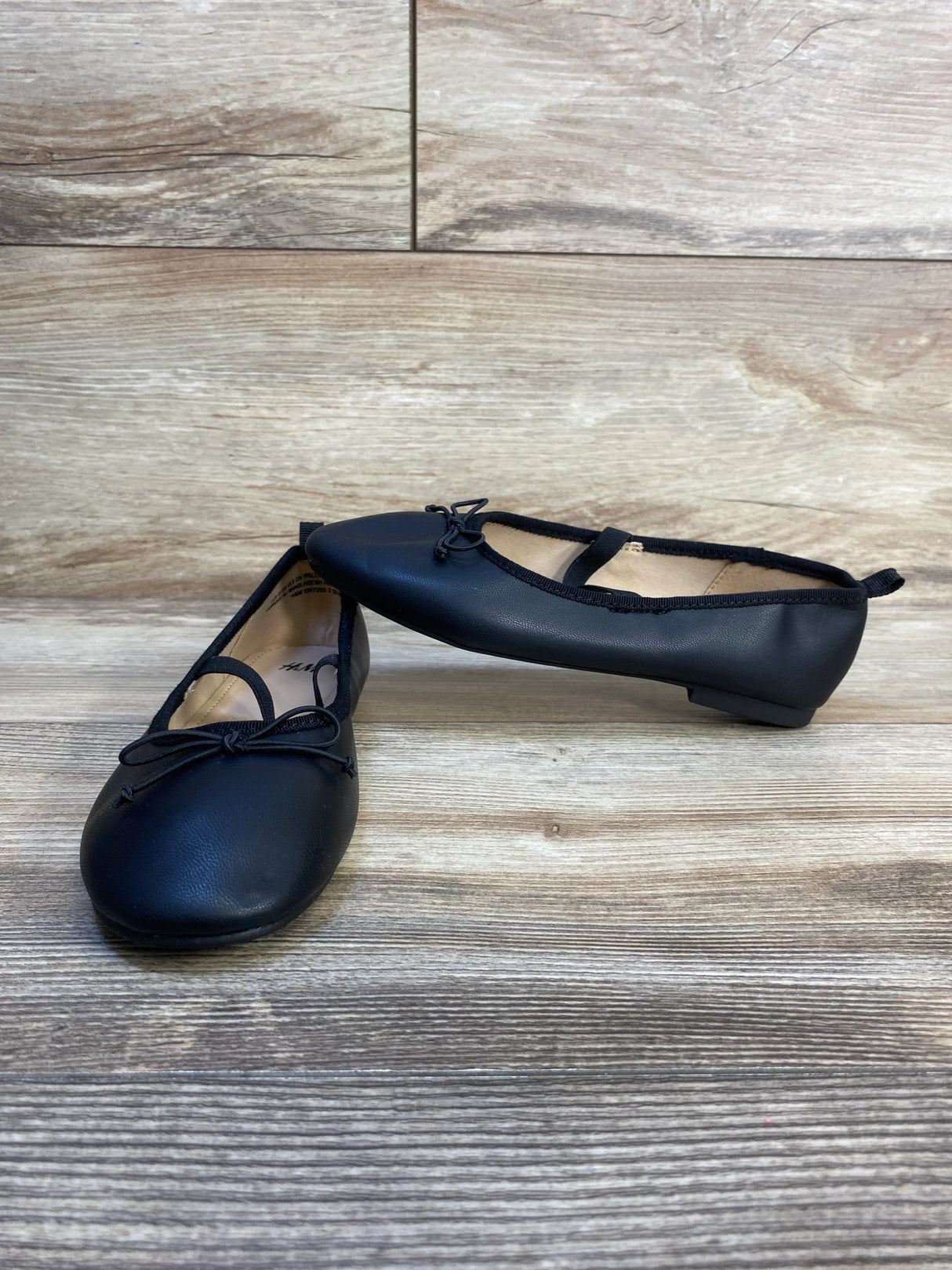 Black girls ballet flats with straps and bow, kids shoes on wood background