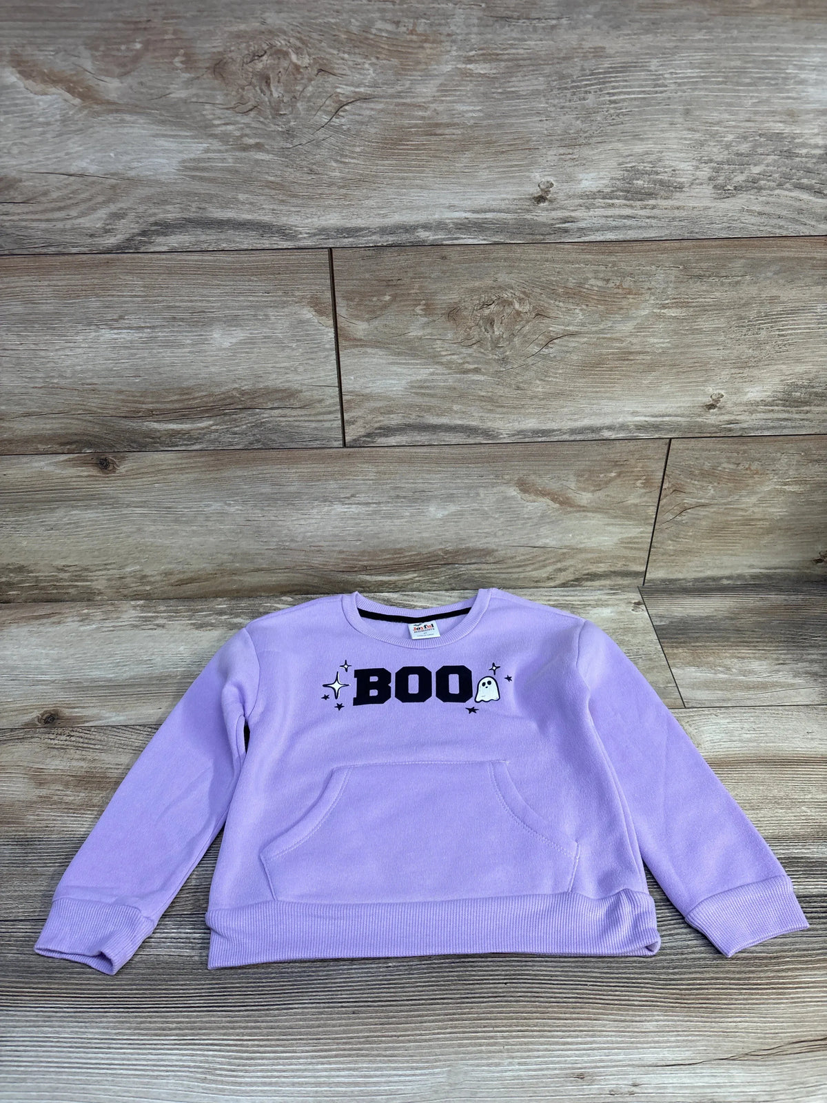 Front of Joyful Moments purple pullover sweatshirt with BOO chest print, ghost icon, and kangaroo pocket on wood background