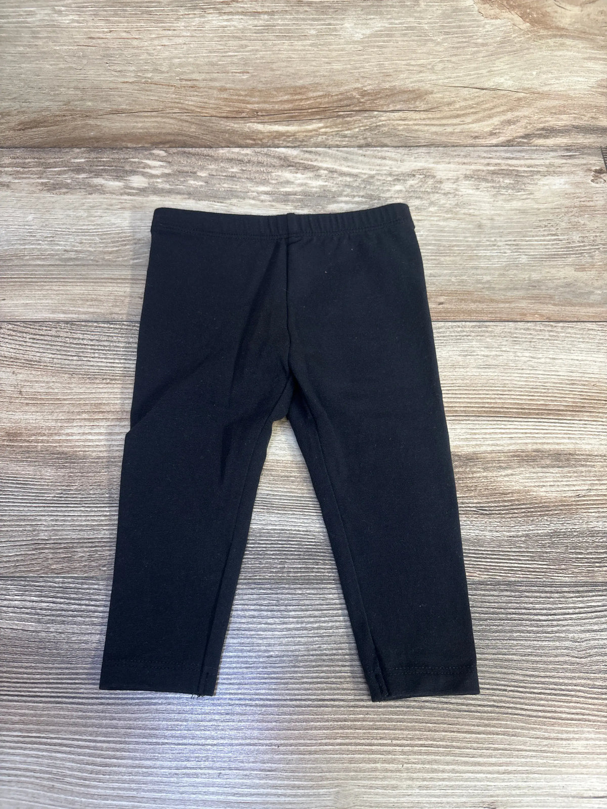 Front view of Jumping Beans black cotton leggings for 12-month-olds showcasing the elastic waistband on a wood-grain background