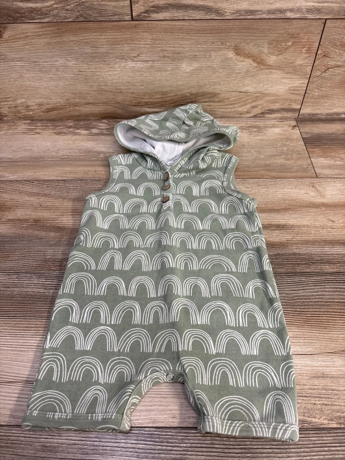 Front view of green hooded Henley shortie romper with white rainbow pattern and front buttons on wood floor
