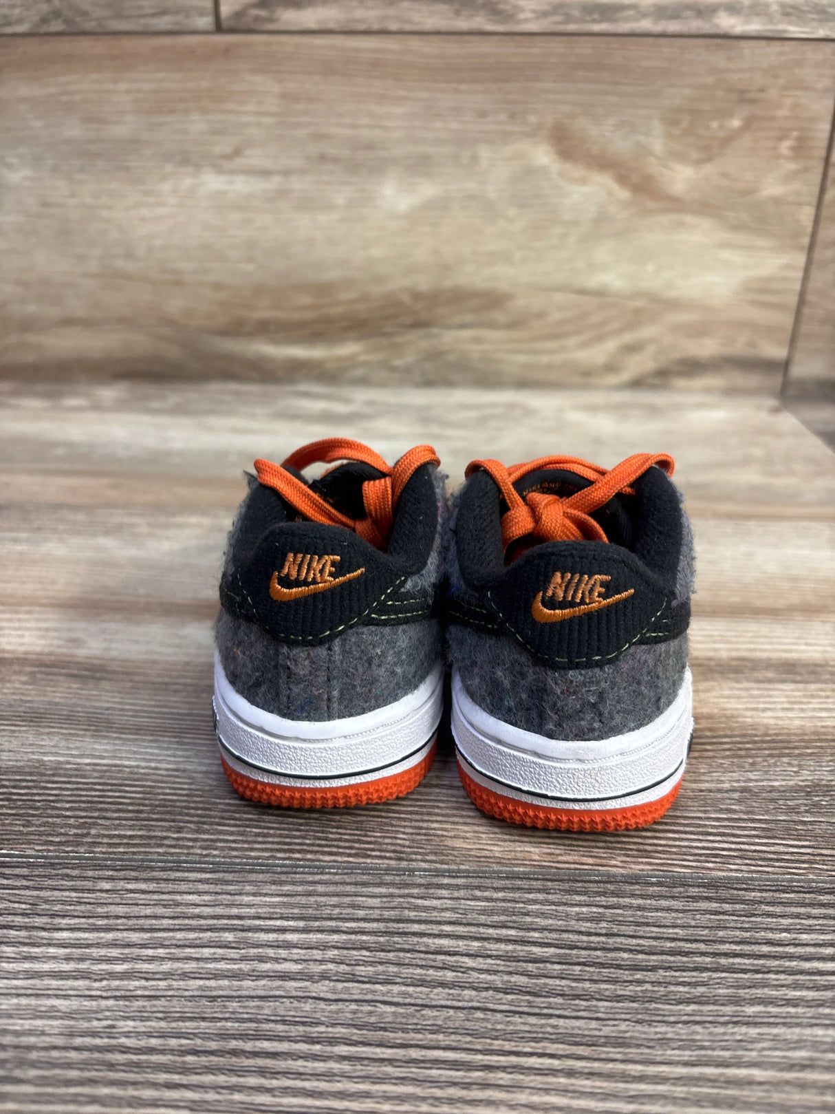 Rear view of toddler Nike Force 1 LV8 TD sneakers showing gray felt upper, orange laces and orange sole on wood background
