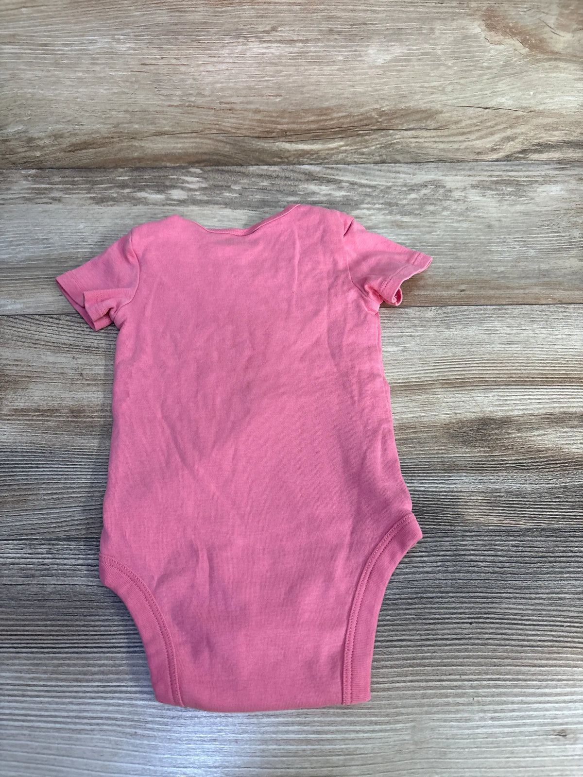 Back view of Okie Dokie bodysuit showcasing plain pink fabric and short sleeves on a wood-grain background