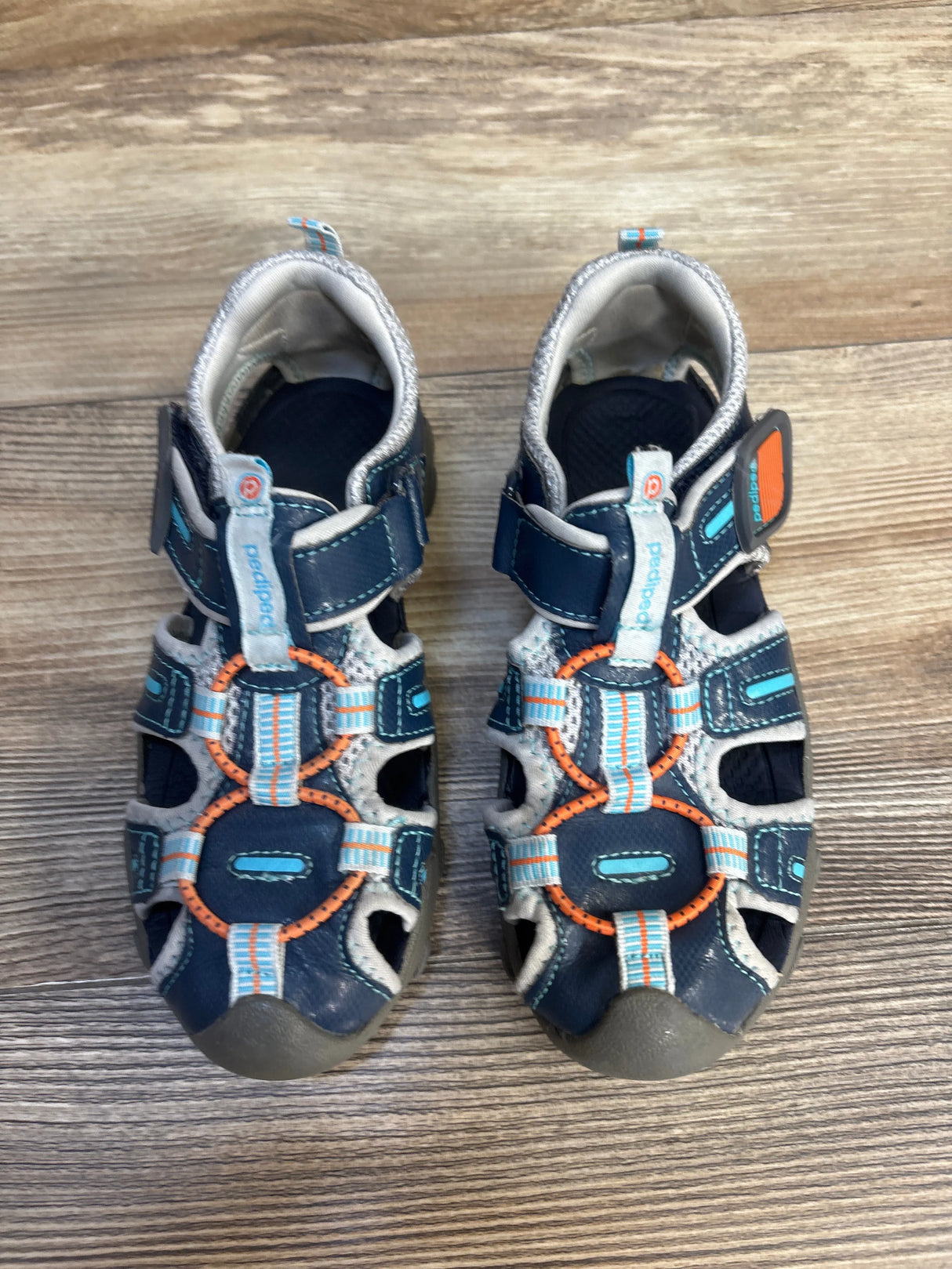Top view of Pediped Flex Canyon water sandals, blue and gray, closed-toe with orange accents and Velcro straps on wood floor