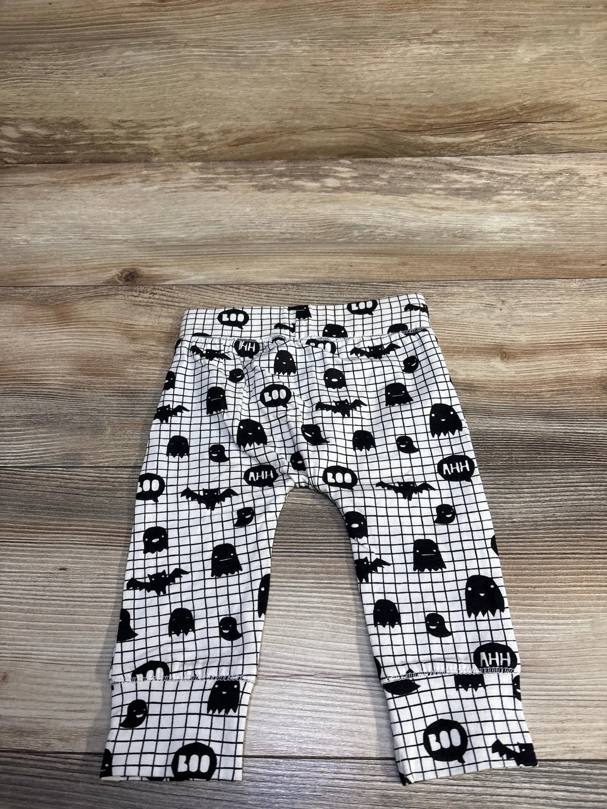 Flat lay of white baby leggings showcasing black grid pattern with ghost and bat motifs and speech bubble print on wood background