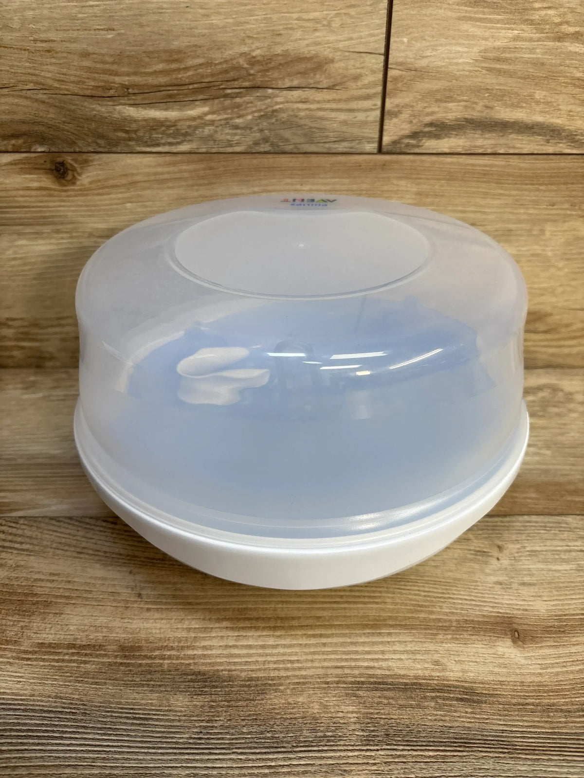 Angled top view of AVENT microwave steam sterilizer showcasing translucent lid and white base on wooden background