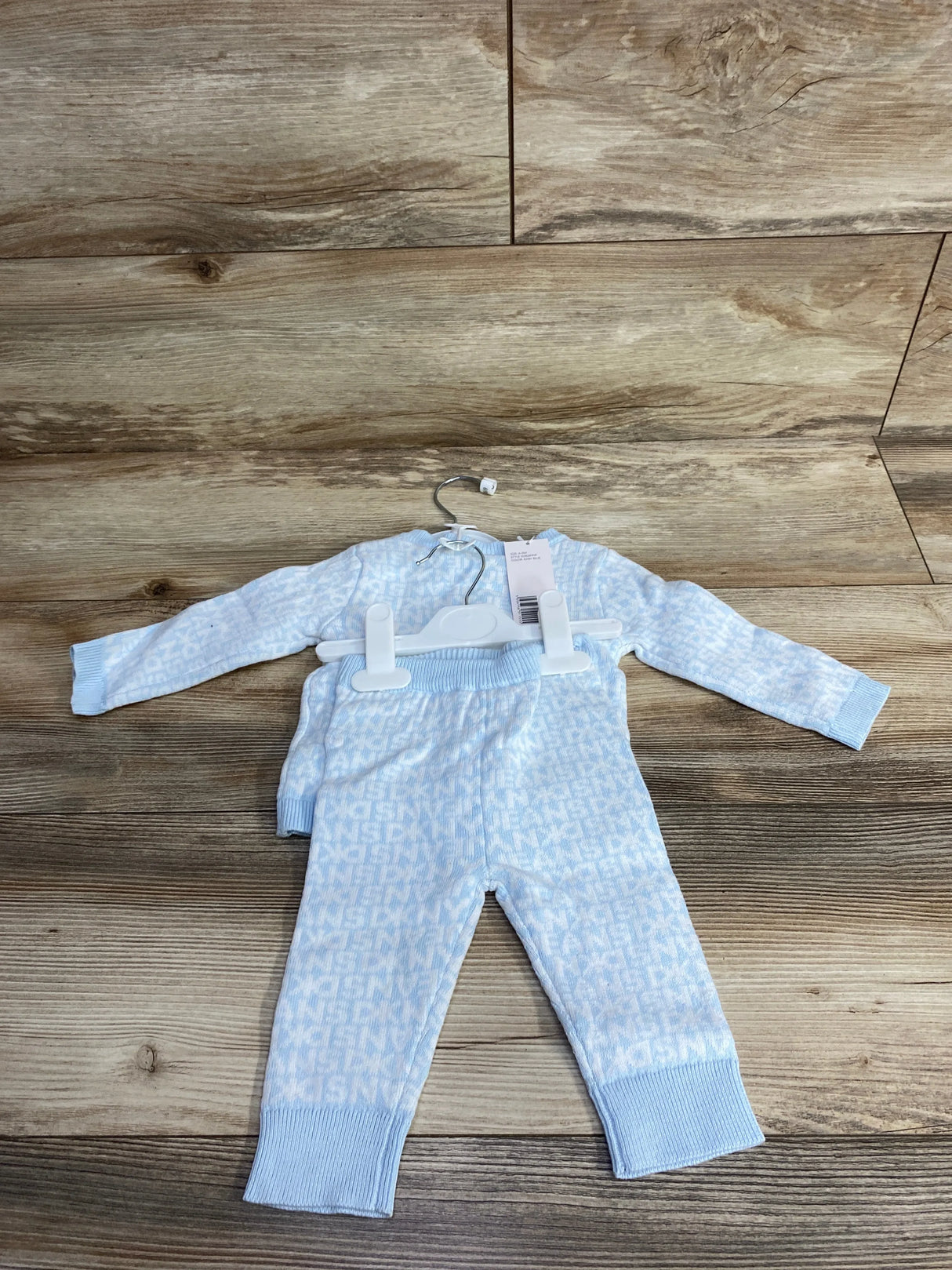 Light blue and white knitted baby sweater and pants set on wooden floor with subtle letter pattern