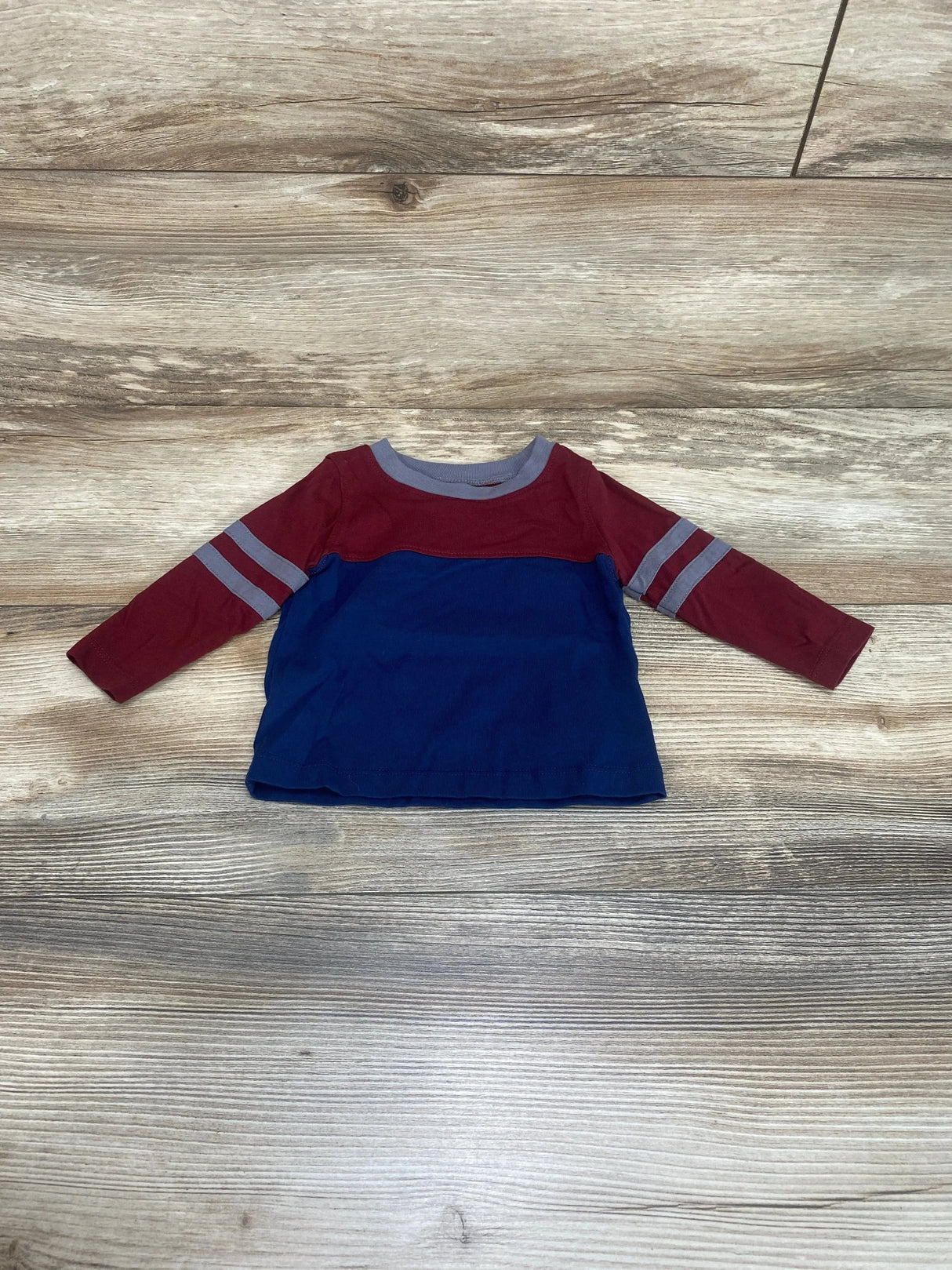 Top-down of baby color-block long-sleeve shirt, size 3-6M; maroon top and sleeves with gray stripes, navy body on light wood