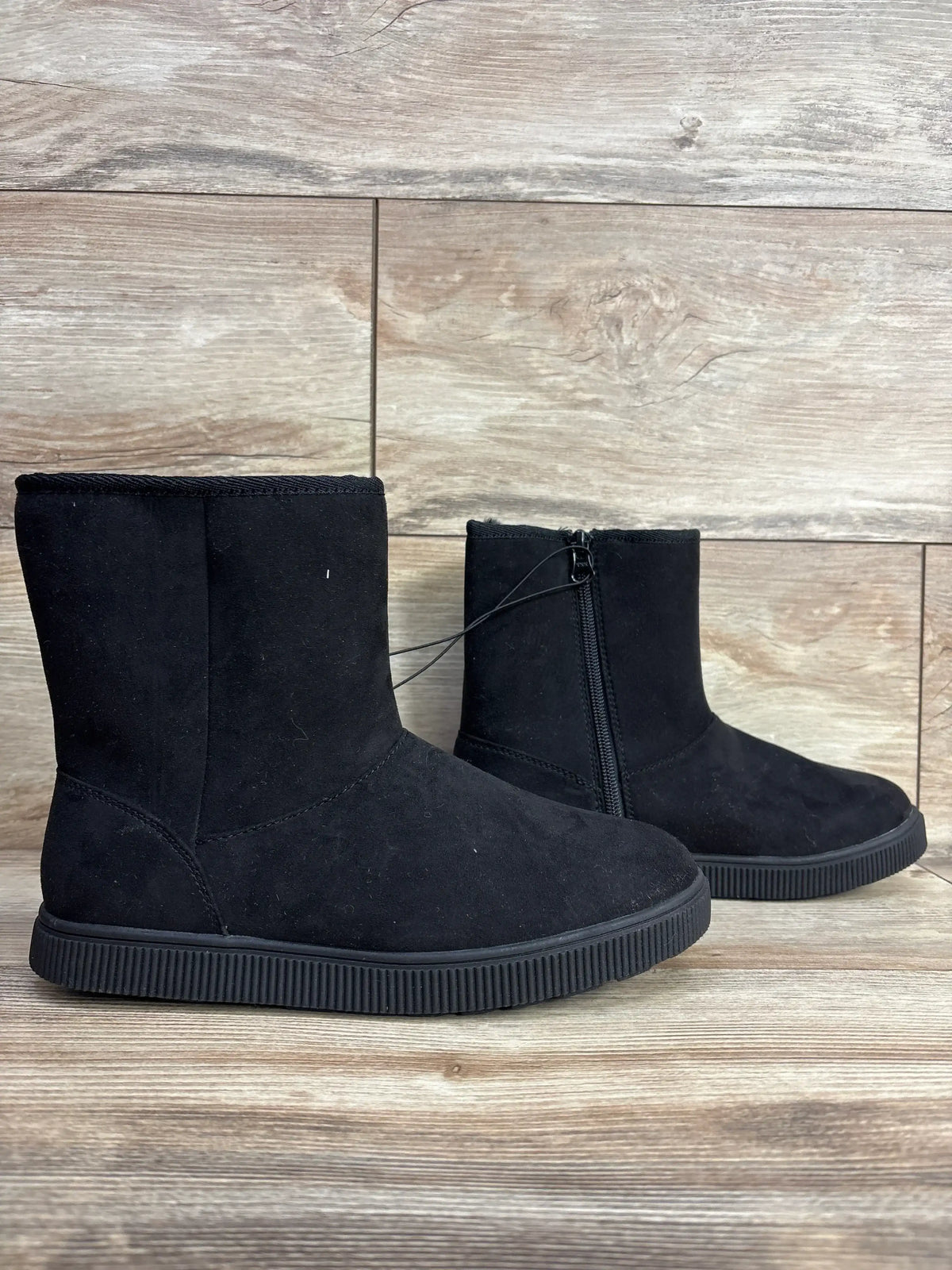 Side view of Cat & Jack Holland shearling-style black kids boots size 4Y showing side zipper and non-slip sole on wood