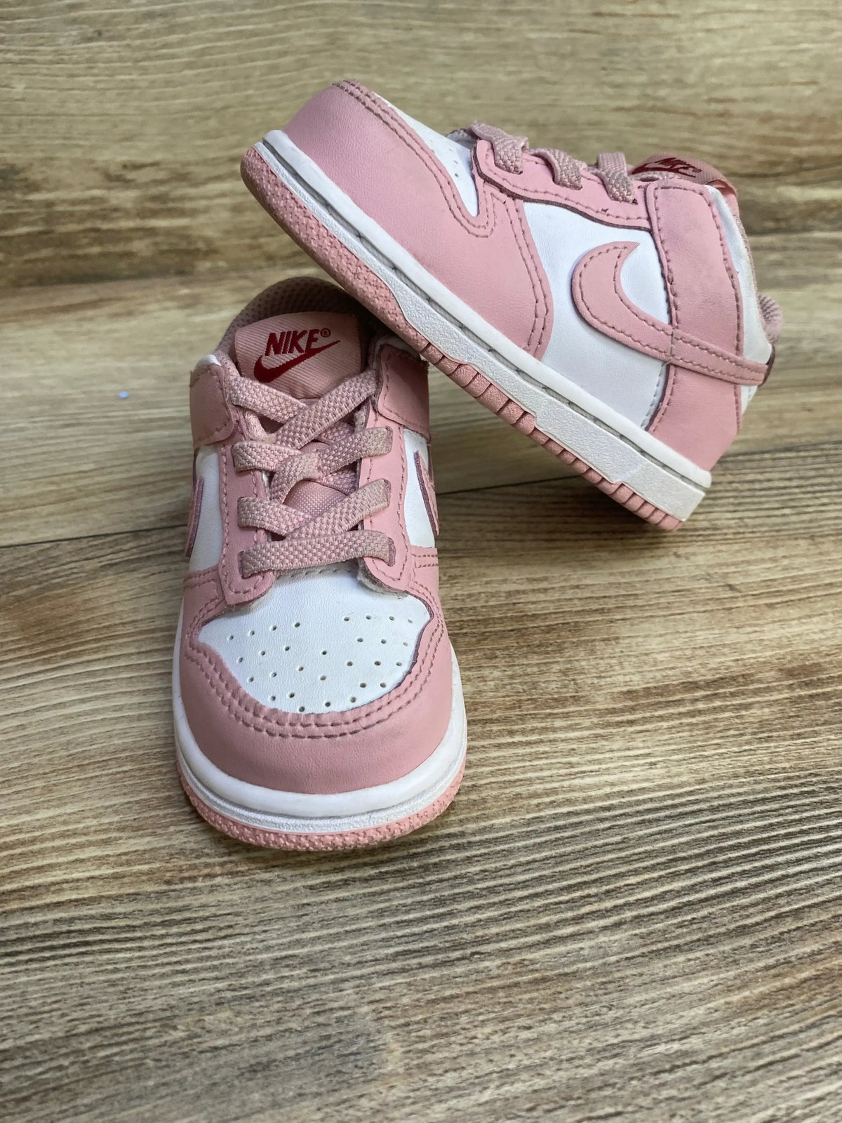 Front and side view of toddler Nike Dunk Low ‘Pink Glaze’ sneakers showcasing pink leather overlays and white panels on a wood floor