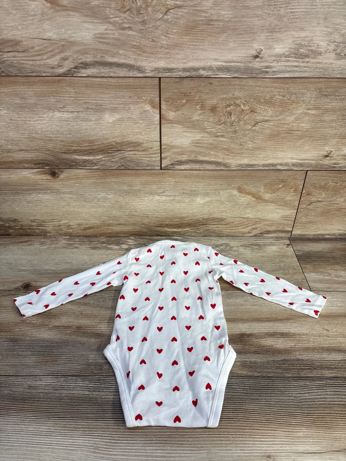Front view of H&M white long sleeve bodysuit with red heart print, size 9 months, laid on a wood background