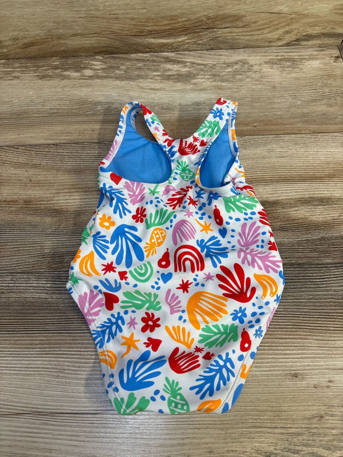 Top view of girls Speedo one piece swimsuit showcasing colorful sea print, blue lining and racerback straps on wood floor