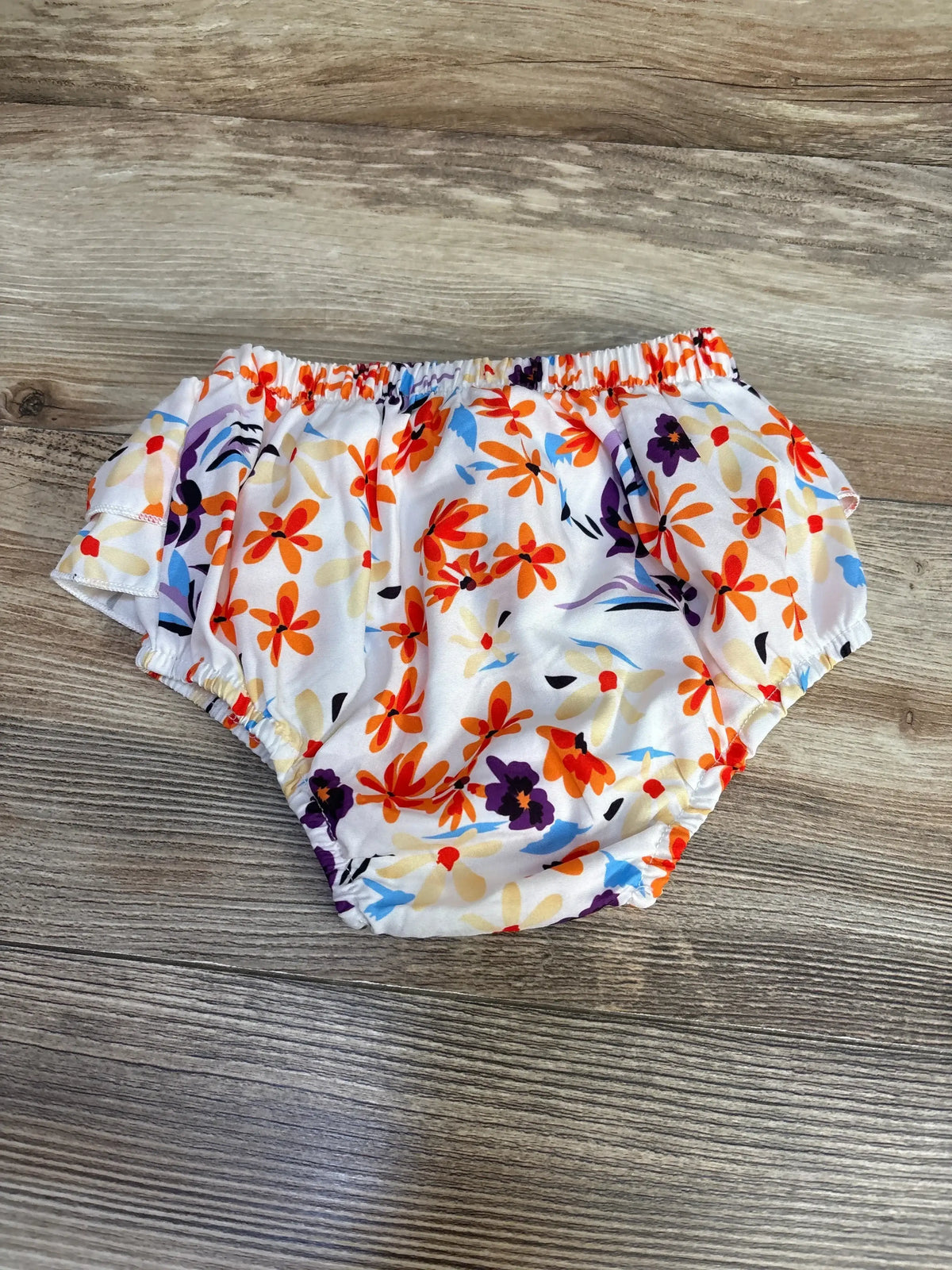 Flat lay of white floral baby bloomers (12-18M) with ruffled waistband and elastic leg openings on wood background